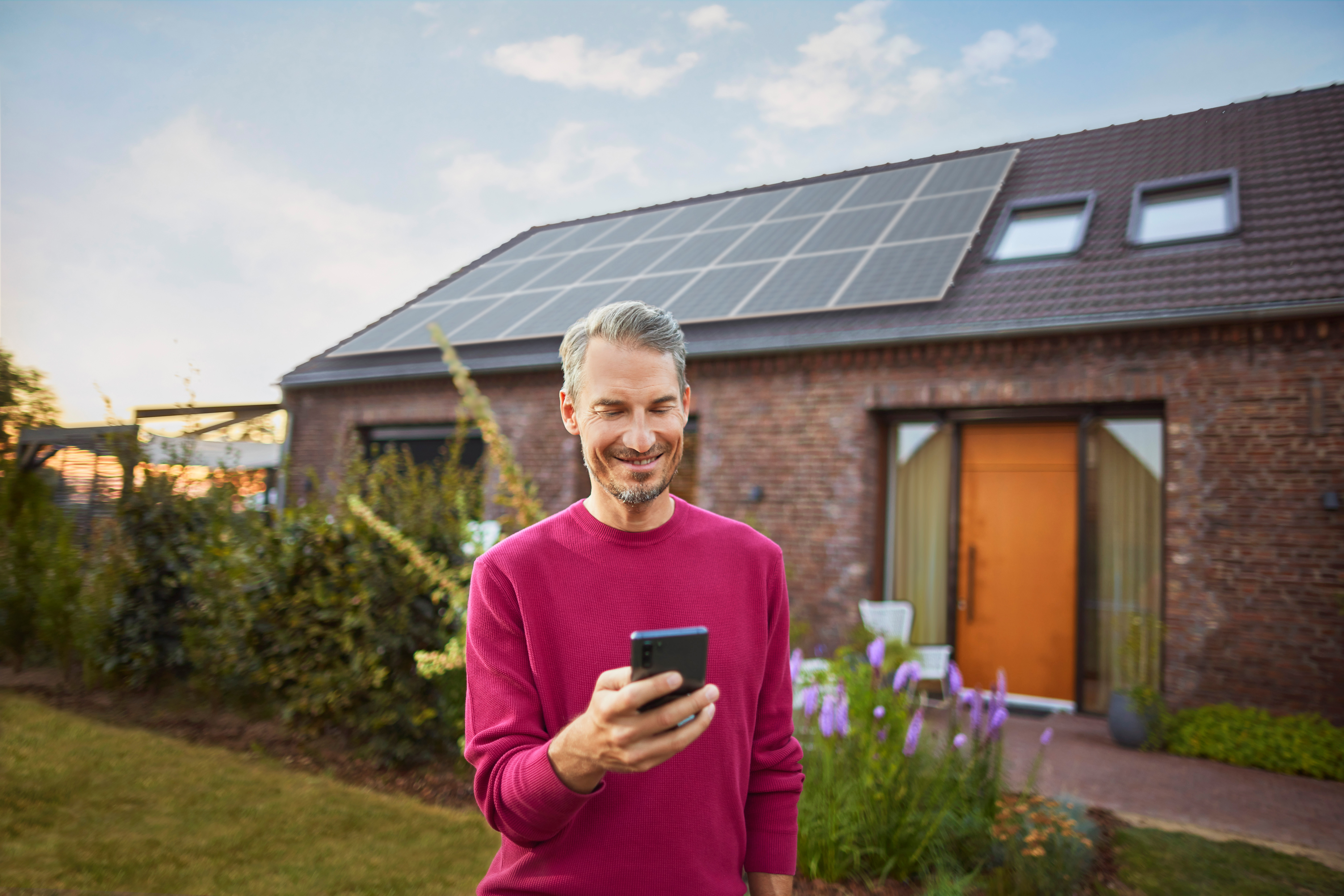 Ein Mann steht mit einem Smartphone im Garten und informiert sich über das Thema Stromerzeugung bei Photovoltaikanlagen bei seinem Energieversorger NEW Energie.