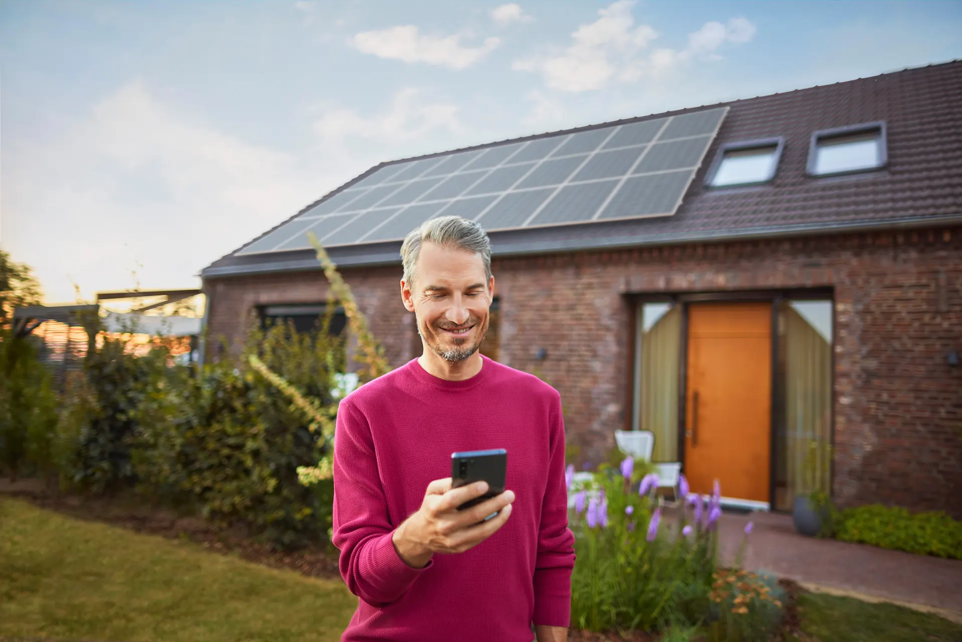 Mann verwendet Smartphone um Angelegenheiten zu klären Ein Mann steht mit einem Smartphone im Garten und informiert sich über das Thema Stromerzeugung bei Photovoltaikanlagen bei seinem Energieversorger NEW Energie.
