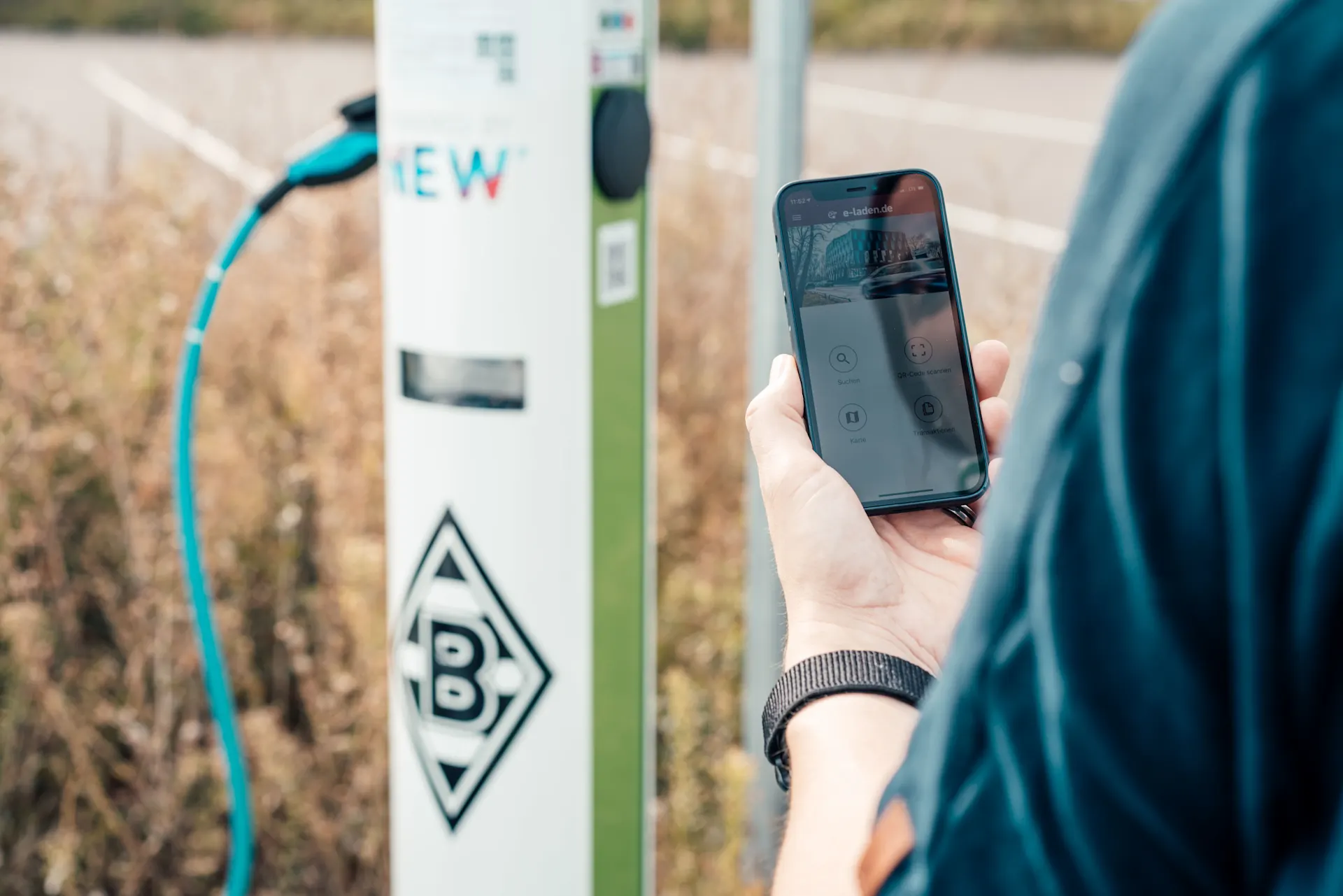 Ladevorgang auswählen Die Frau hat auf ihrem Handy eine App fürs E-Laden geöffnet während sie an einer Ladestation der NEW steht.