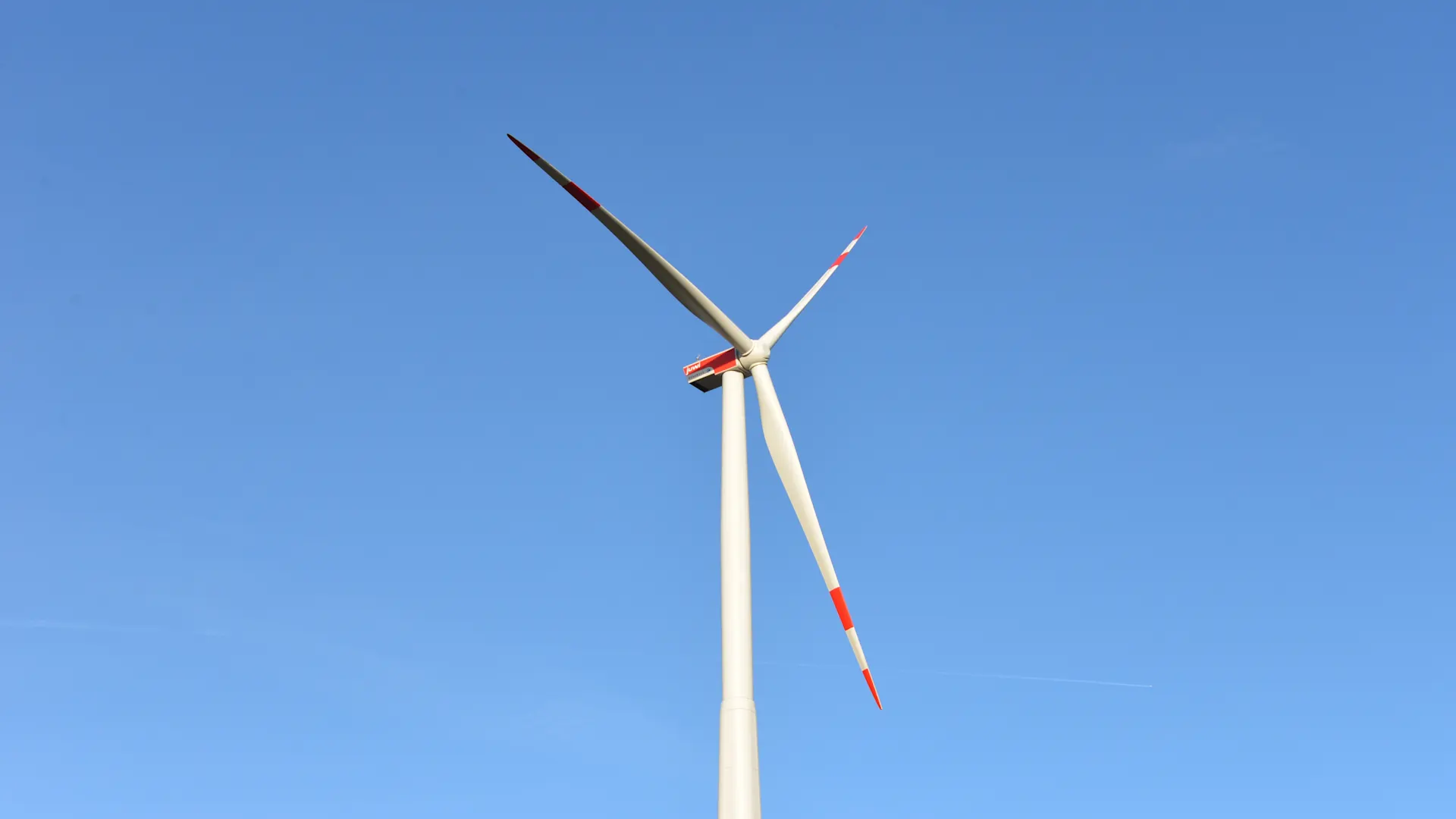 Windenergie Blick auf ein Windrad. Im Hintergrund ist ein klarer blauer Himmel zu sehen.