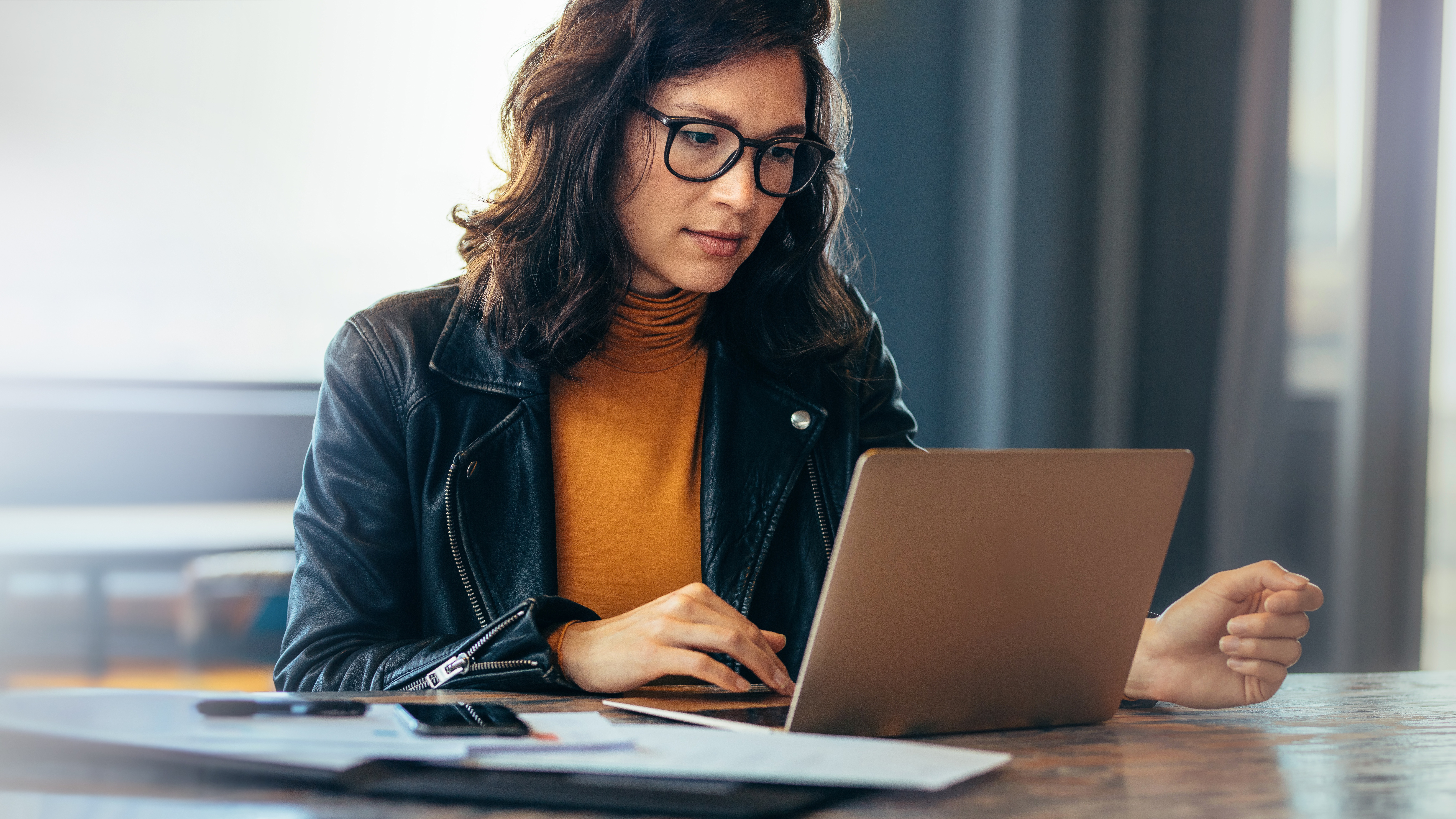 Eine Frau mit schwarzer Brille sitzt am Tisch vor ihrem Laptop und schaut sich die NEW Energie an.