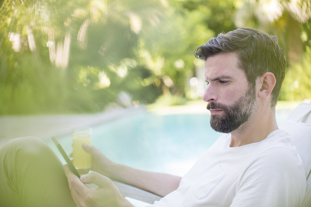 Ein Mann sitzt an einem Pool mit seinem Handy und einem Getränk in der Hand. Dabei schaut er nach Stromtarifen der NEW Energie. 