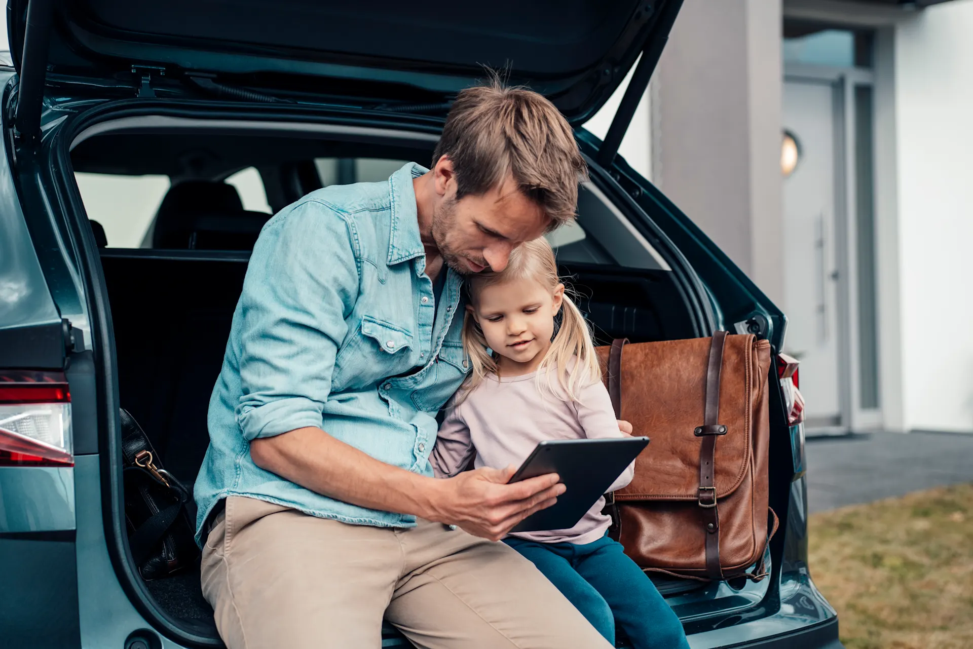 Familie im offenen Kofferraum Mädchen und Vater sitzen im Kofferraum des E-Autos und vergleichen Tarife bei der NEW Energie.
