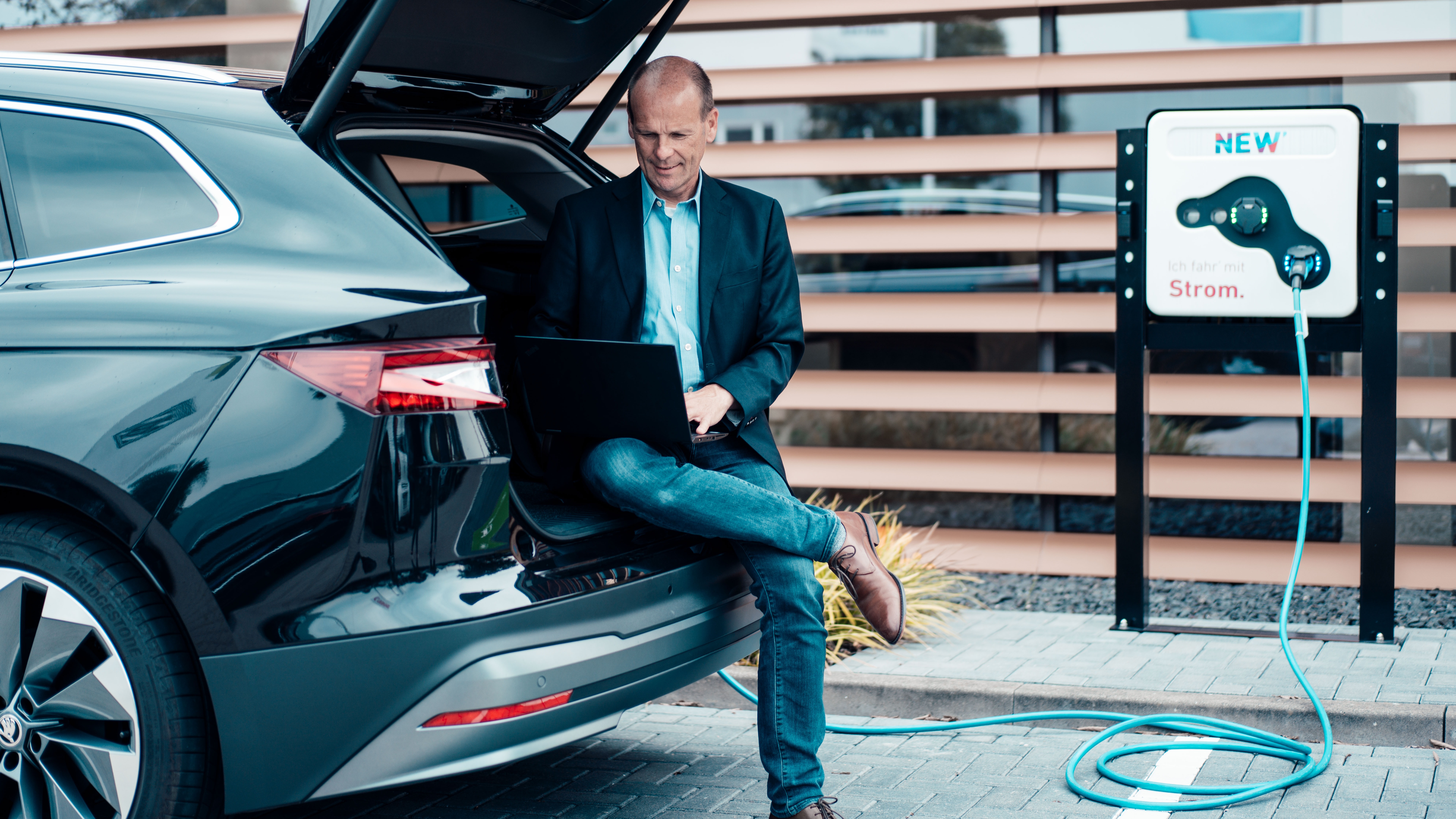 Ein Unternehmer sitzt in dem Kofferraum eines E-Autos an seinem Laptop und schaut nach dem Service der NEW Energie.