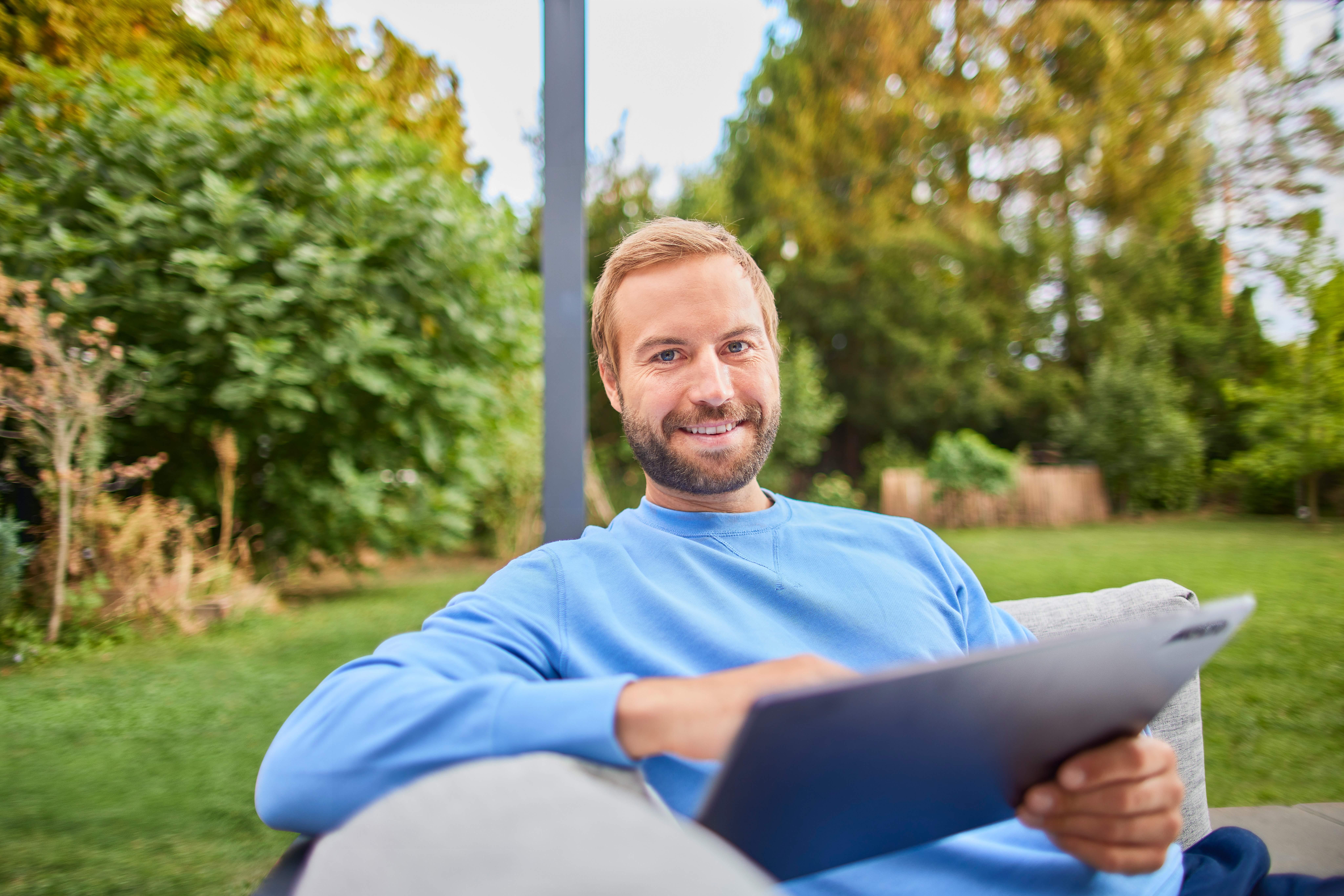 Ein Mann sitzt mit seinem Tablet im Garten und vergleicht Stromtarife der NEW Energie.