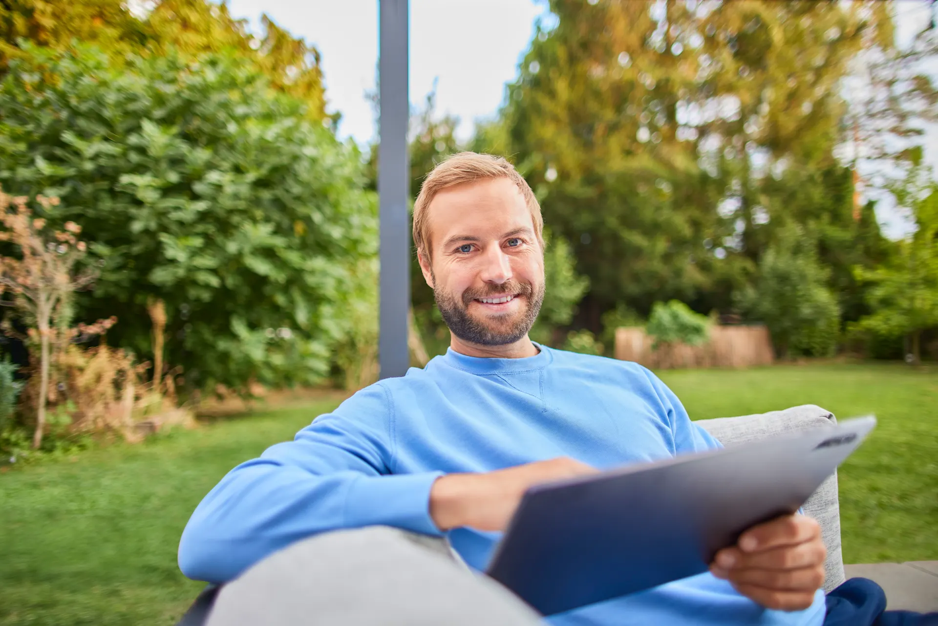 NEW Services entdecken Ein Mann sitzt mit seinem Tablet im Garten und vergleicht Stromtarife der NEW Energie.