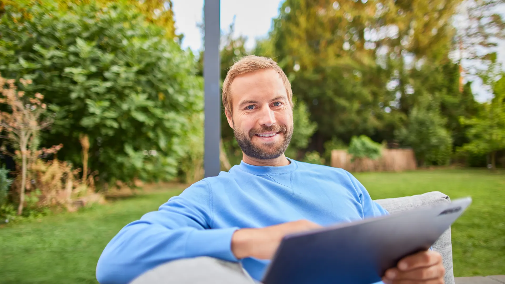 NEW Services entdecken Ein Mann sitzt mit seinem Tablet im Garten und vergleicht Stromtarife der NEW Energie.
