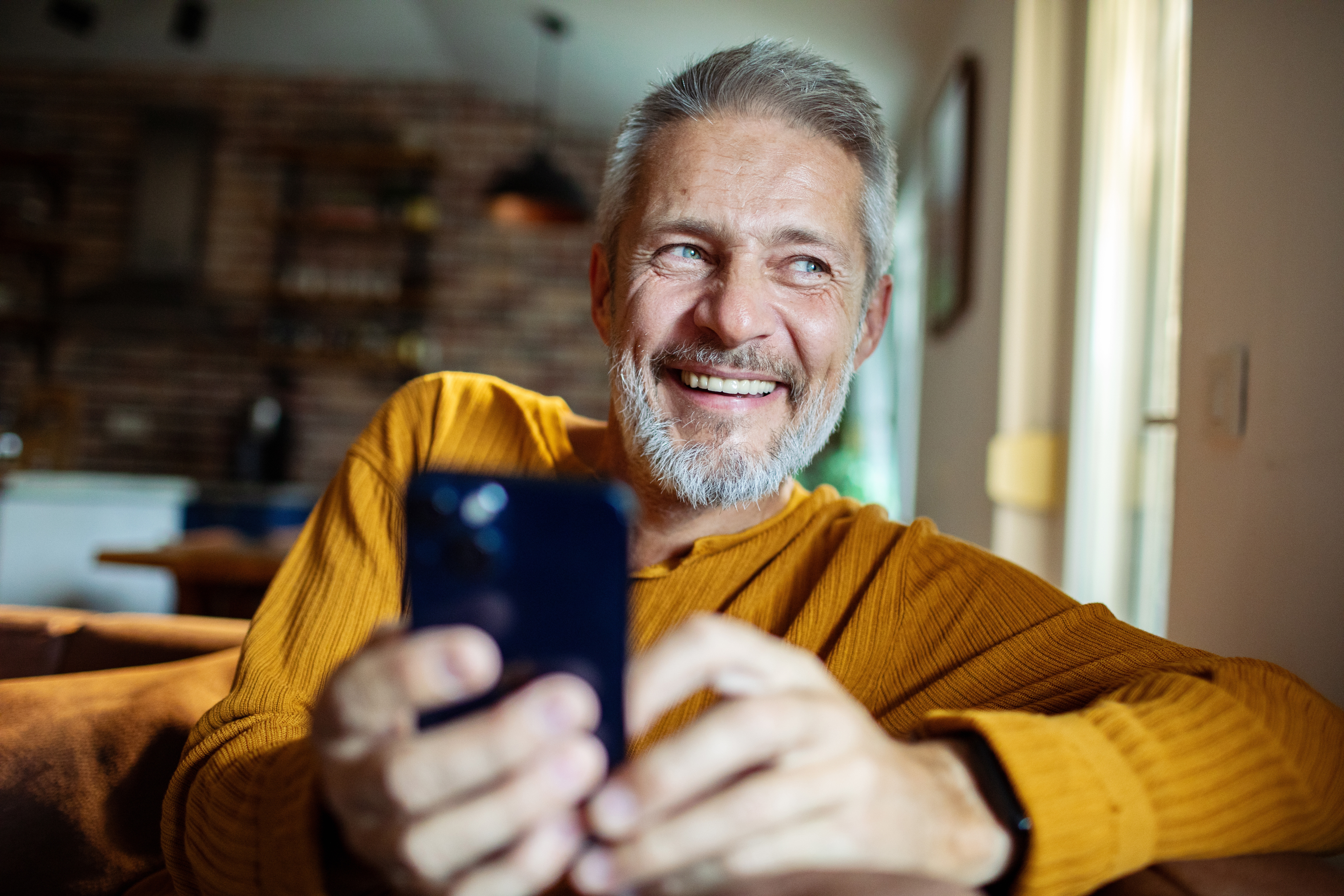 Ein Mann sitzt mit seinem Smartphone im Wohnzimmer und denkt über die zuverlässige Versorgung der NEW Energie nach.