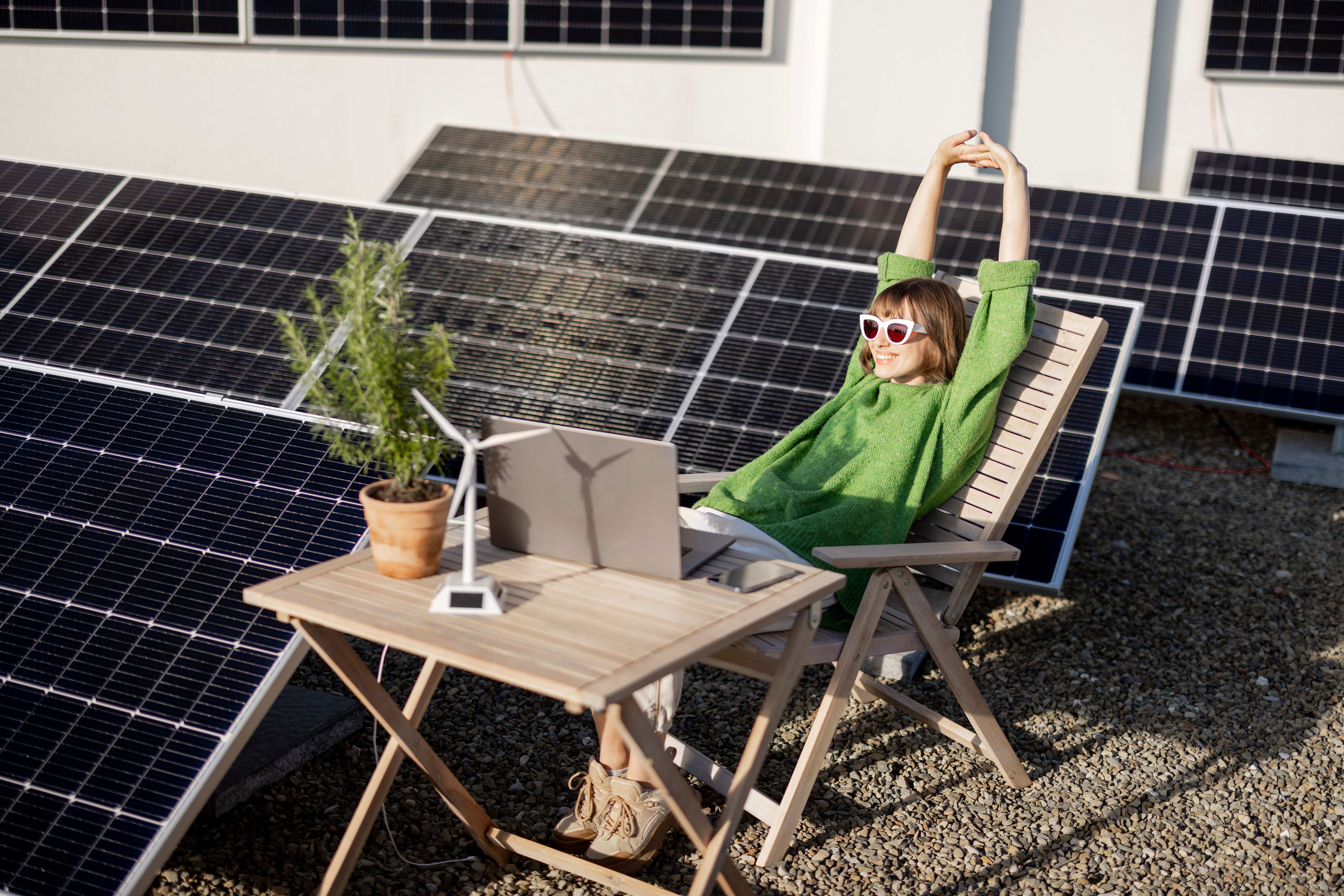 Die Frau sitzt neben einer Photovoltaikanlage der NEW Energie auf dem Dach.