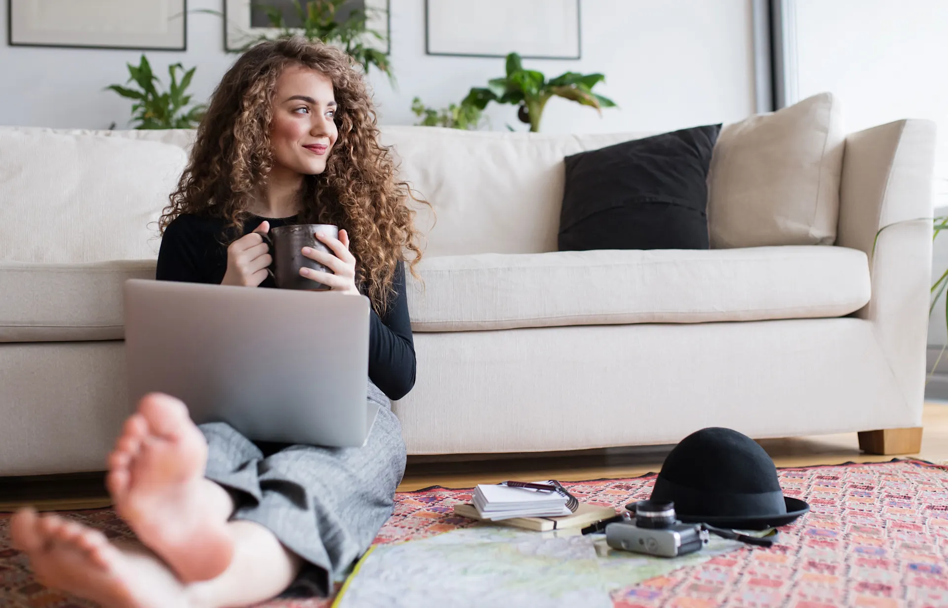 Frau mit Laptop und Kaffee Frau mit Laptop und Kaffee sitzt entspannt vor dem Sofa auf dem Boden und schaut Tarife der NEW-Energie.