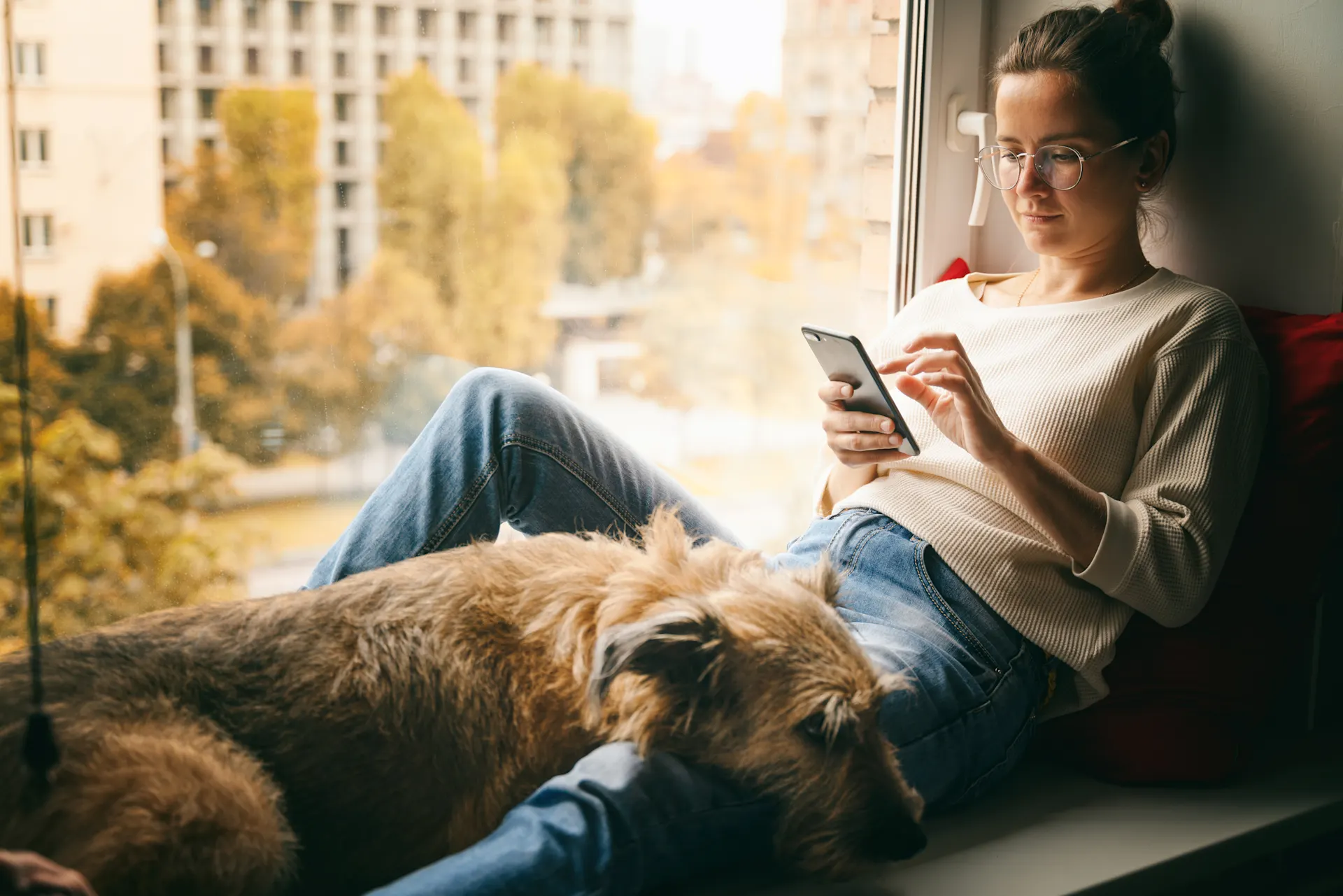 Frau sitzt mit ihrem Smartphone auf einem Fensterbrett und prüft die Angebote und Services der NEW Energie.