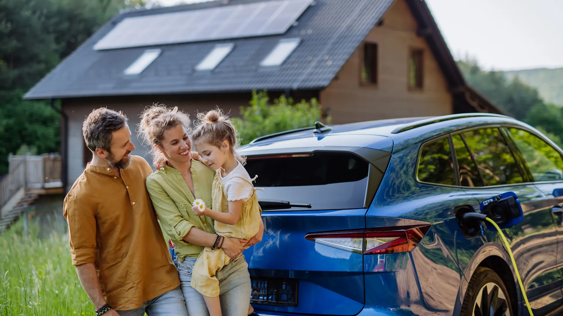 Familienzeit mit der NEW Energie Eine Familie steht vor ihrem E-Auto. Im Hintergrund steht ihr Haus mit einer PV-Anlage der NEW Energie. Ebenfalls beziehen Sie Strom und Gas von der NEW Energie.
