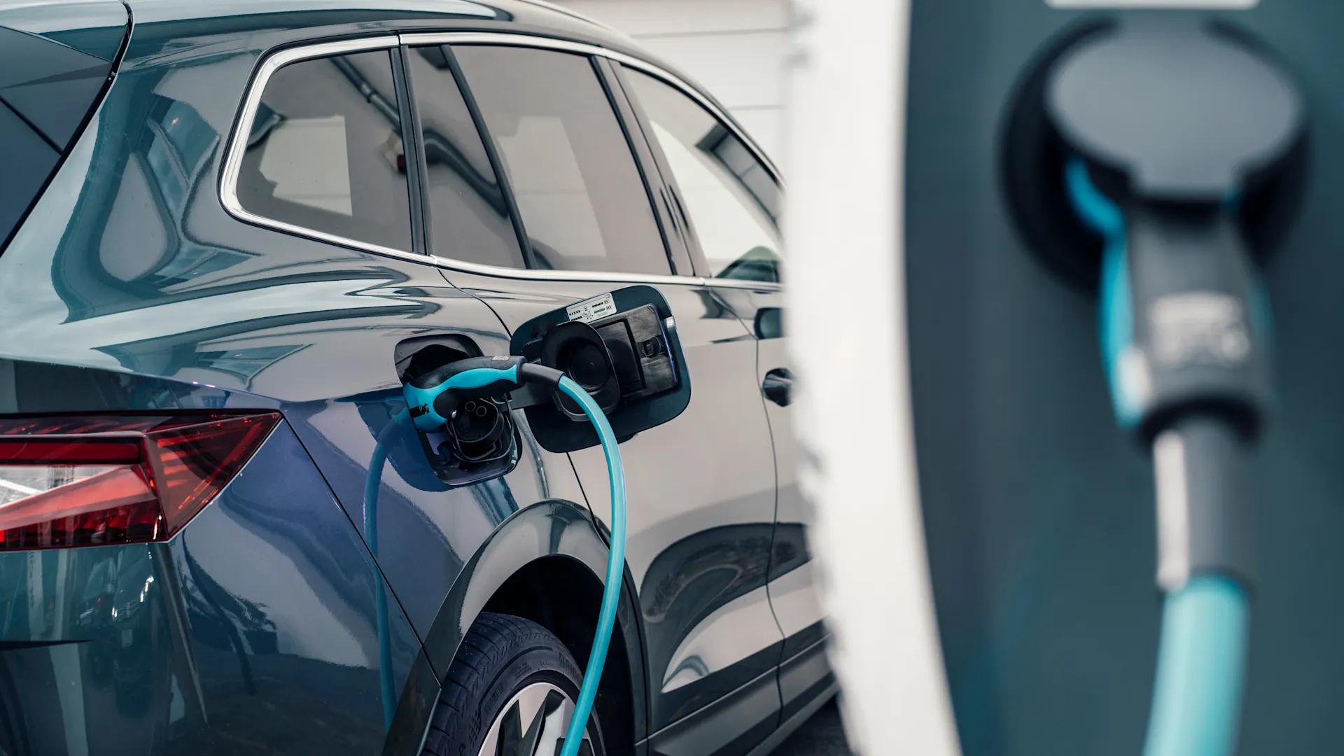 Günstige Autostromtarife Ein E-Auto steht vor einem Haus und wird über einen Ladestecker mit der Wallbox verbunden. Der Autostrom kommt von der NEW Energie.