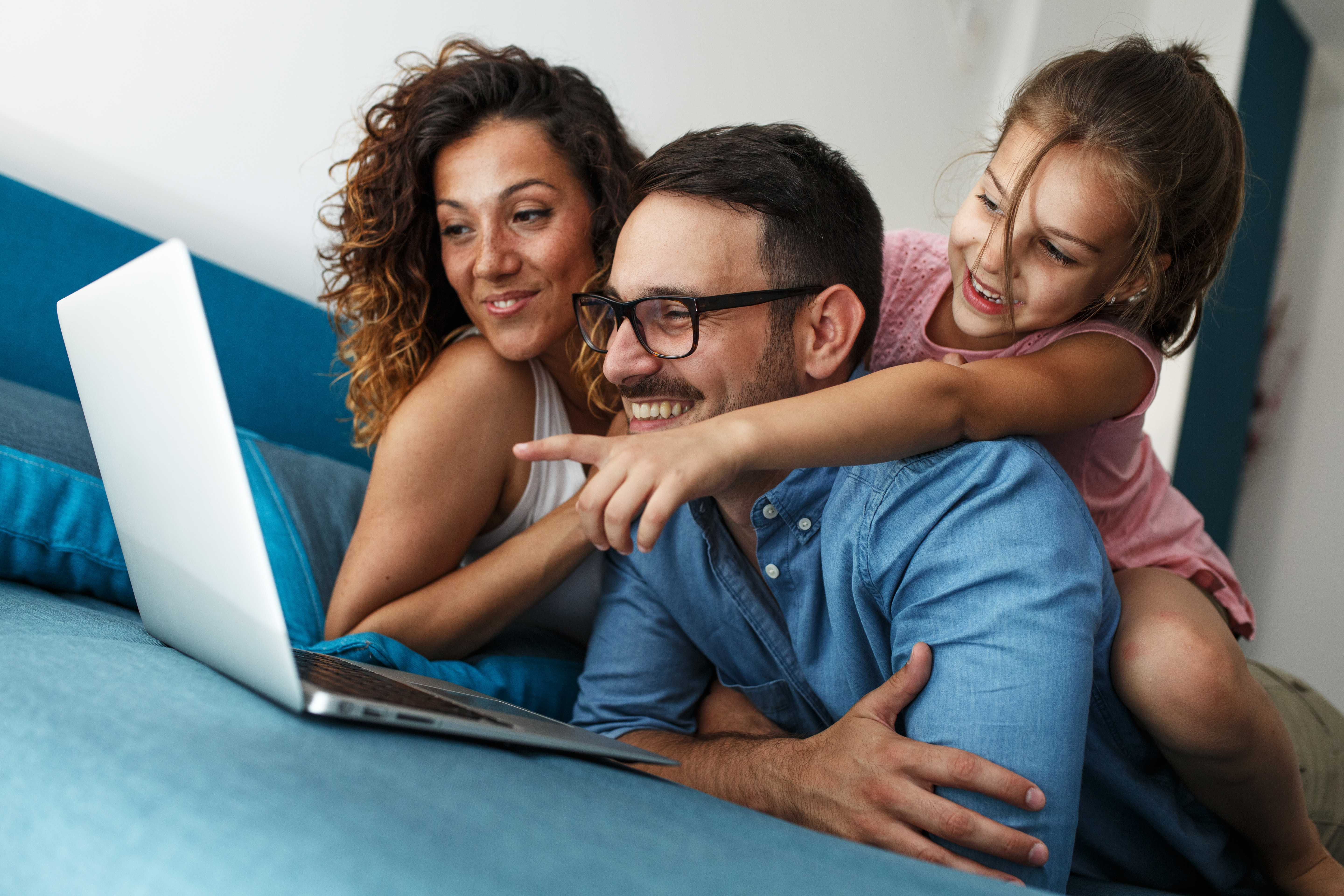 Eine Familie sitzt zusammen auf dem Sofa und schaut sich die Tarife der NEW Energie an. Ein Mädchen zeigt aufgeregt auf den Laptop.