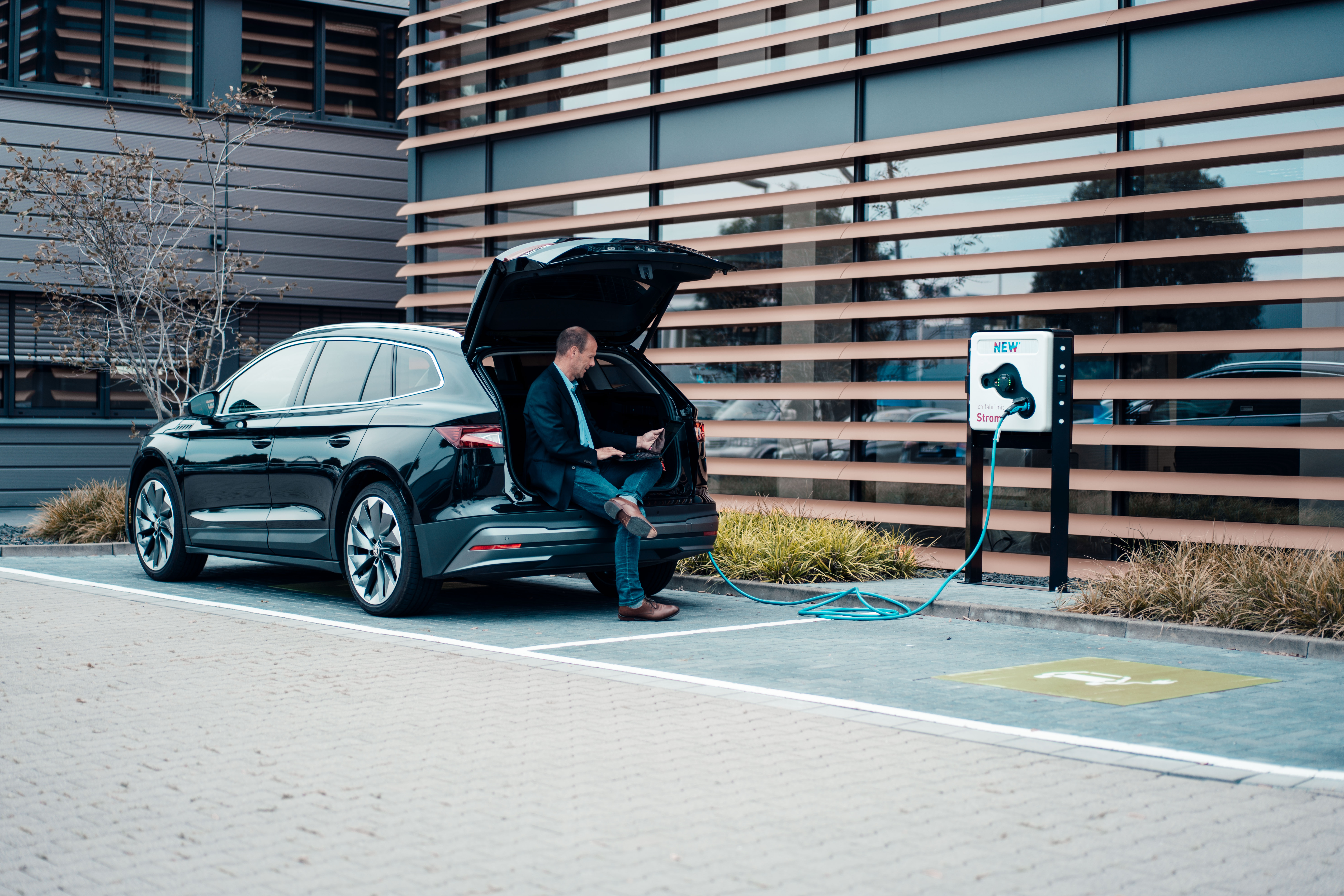 Unternehmer sitzt in seinem Auto und wartet während sein E-Auto an einer Wallbox der NEW Energie lädt.