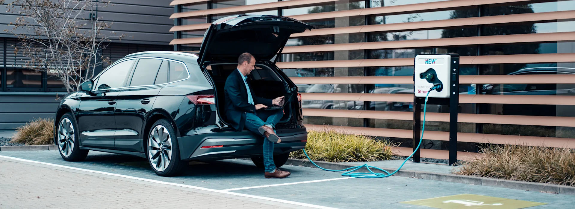 Ladendes E-Auto Unternehmer sitzt in seinem Auto und wartet während sein E-Auto an einer Wallbox der NEW Energie lädt.
