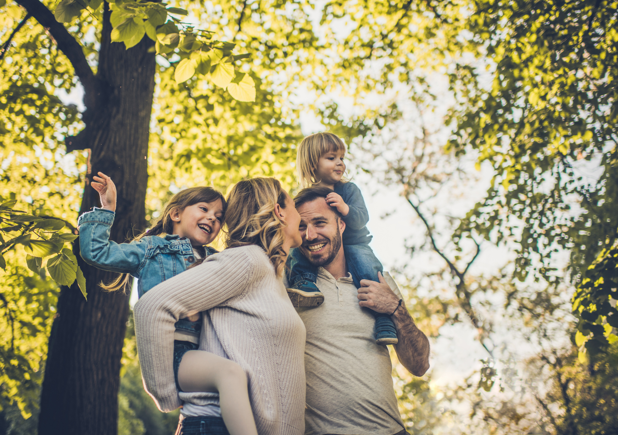 Eine Familie mit zwei Kindern ist sehr naturverbunden und befindet sich im Wald. Vater und Mutter tragen ihre Kinder auf dem Rücken. Sie nutzen Ökostrom der NEW Energie.