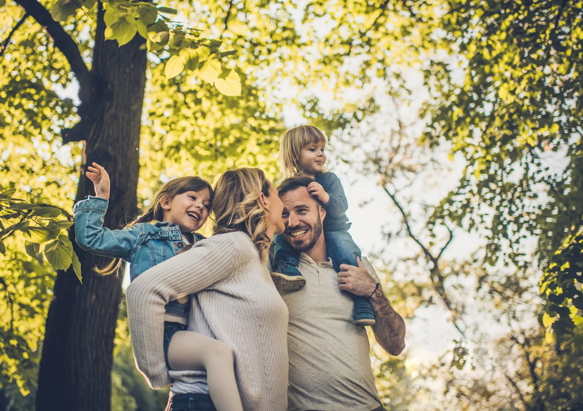 Auswahl von günstigem Ökostrom Eine Familie mit zwei Kindern ist sehr naturverbunden und befindet sich im Wald. Vater und Mutter tragen ihre Kinder auf dem Rücken. Sie nutzen Ökostrom der NEW Energie.