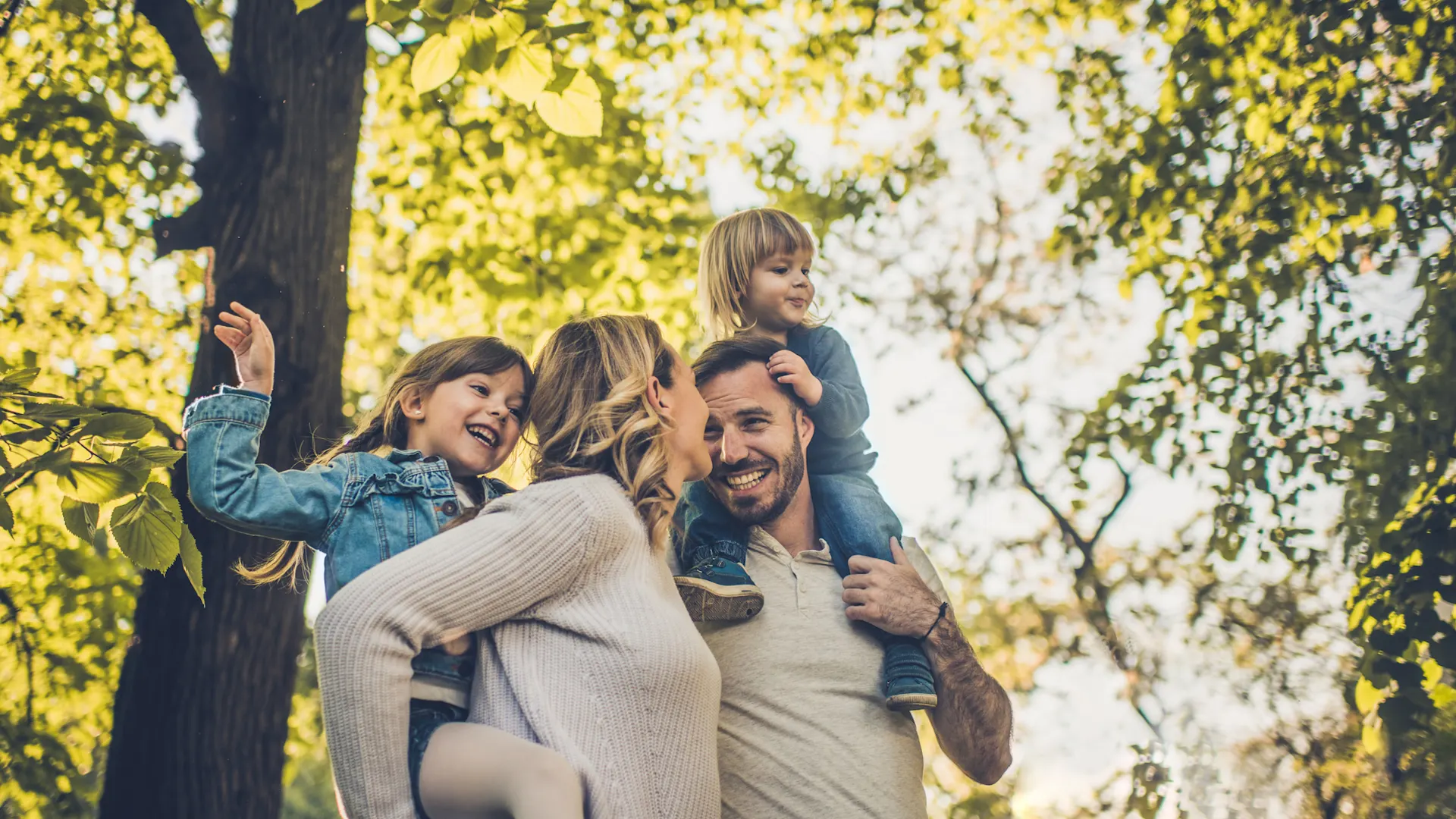 Auswahl von günstigem Ökostrom Eine Familie mit zwei Kindern ist sehr naturverbunden und befindet sich im Wald. Vater und Mutter tragen ihre Kinder auf dem Rücken. Sie nutzen Ökostrom der NEW Energie.