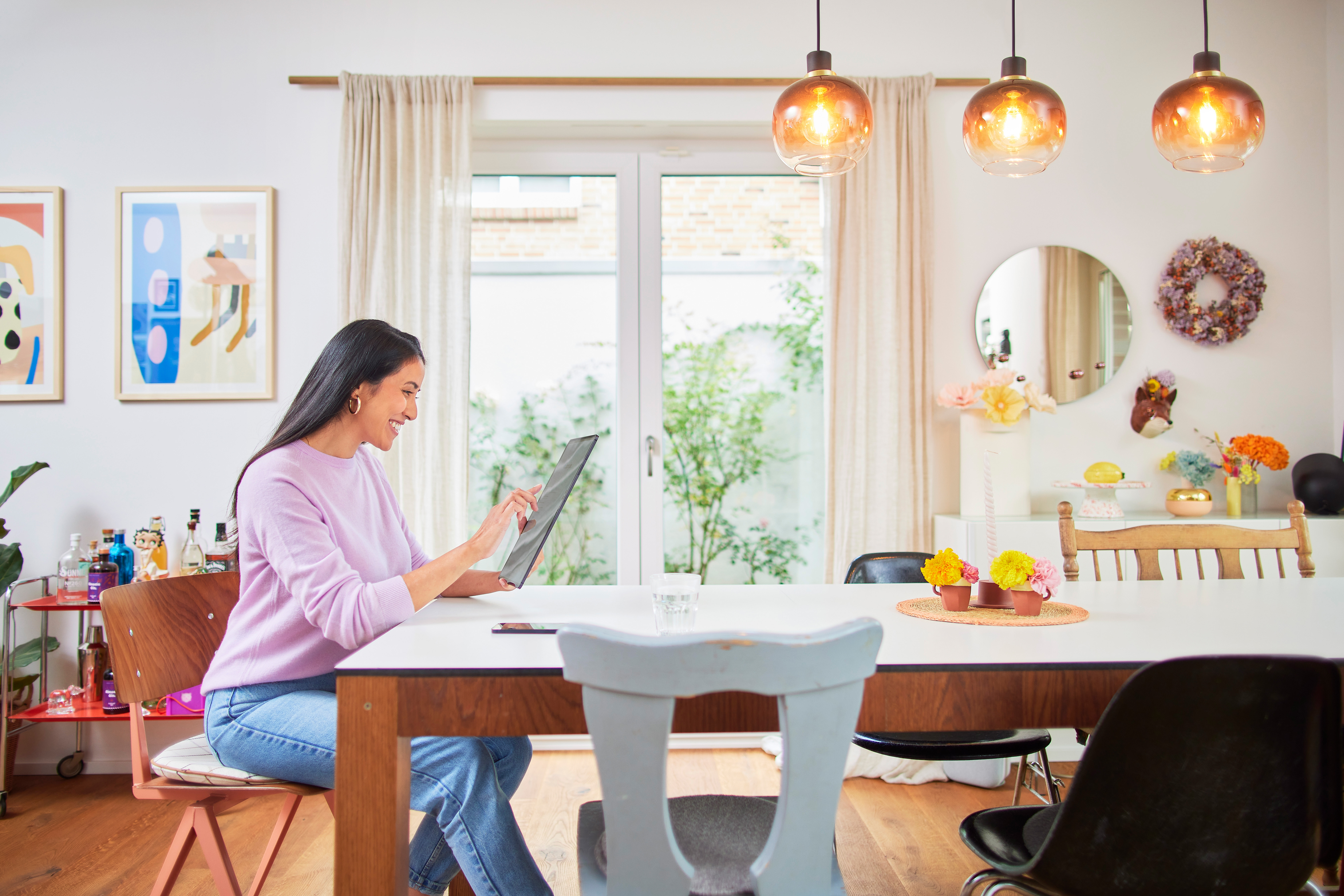Eine Frau sitzt am Esstisch und schaut sich auf ihrem Tablet die günstigen Tarife des Energieversorgers NEW Energie an. 