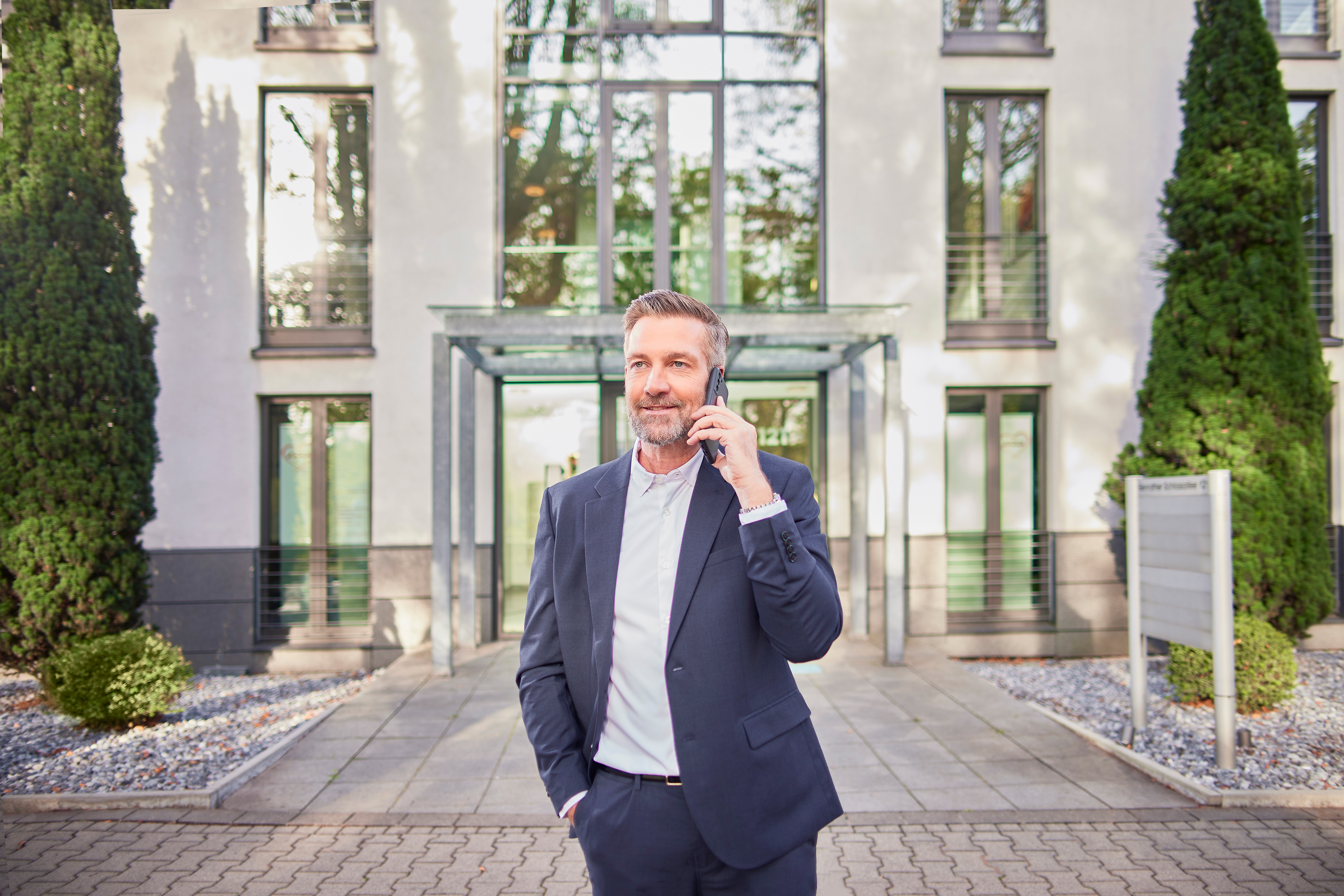 Ein Mann im Anzug steht vor einem Gebäude und telefoniert.
