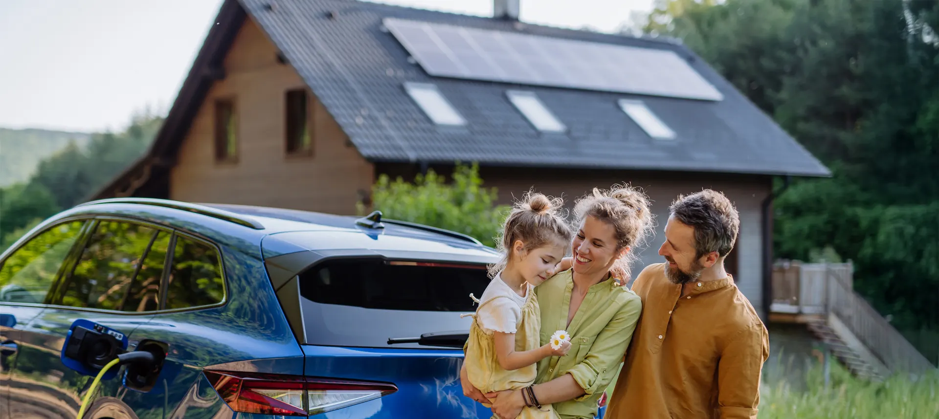 Familie steht vor Ihrem Haus mit einer PV-Anlage auf dem Dach Familie steht vor einem mit Haus im Grünen, mit einer PV-Anlage auf dem Dach und einem Elektroauto davor.