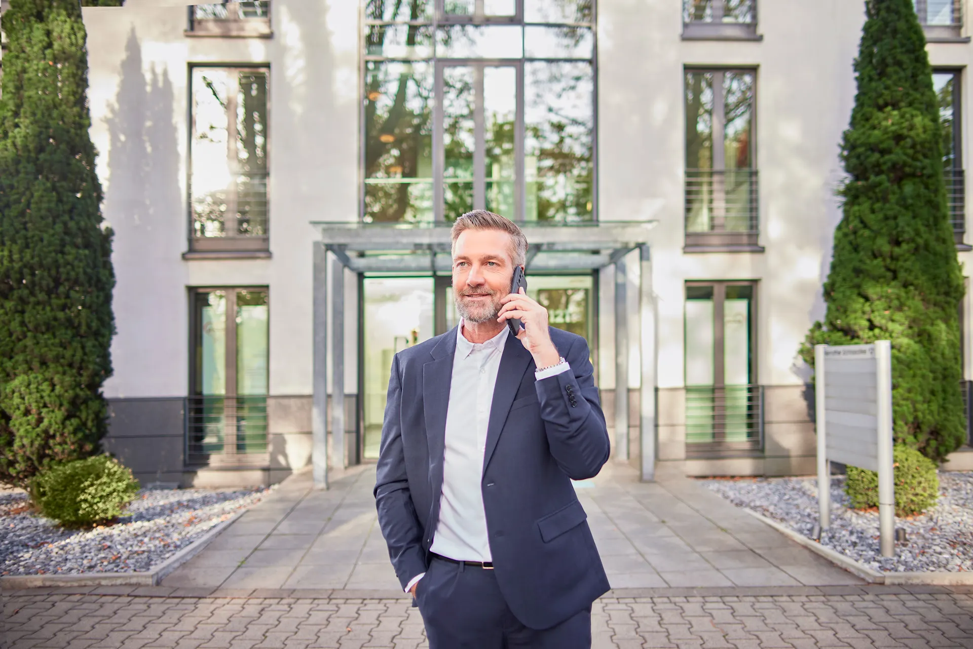 Ein Mann im Anzug steht telefonierend mit der NEW Energie vor einem Mehrfamilienhaus.