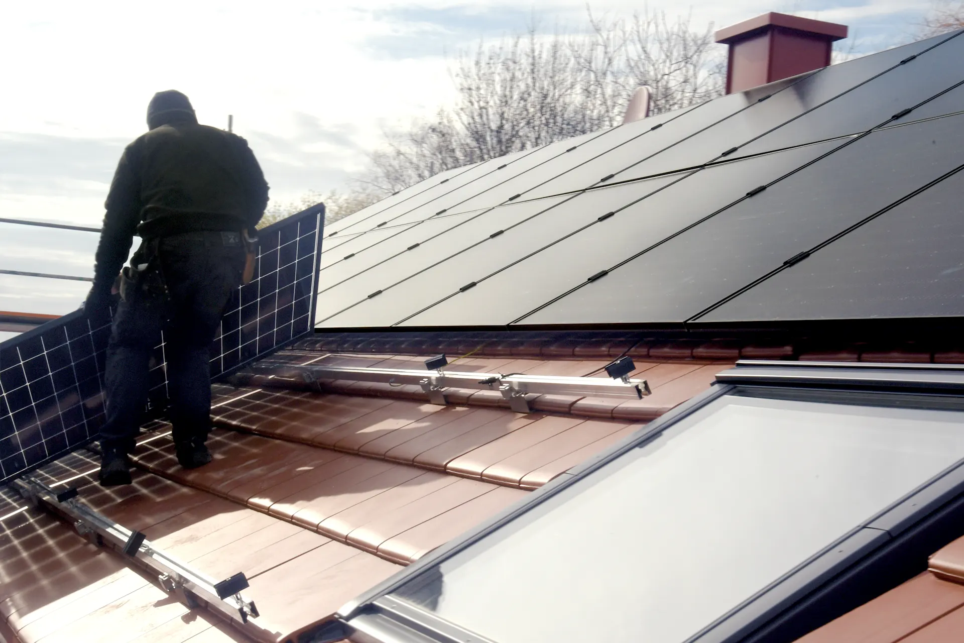 Mann montiert eine Photovoltaikanlage Ein Mann steht auf einem Dach und montiert eine PV Anlage von der NEW Energie zur Herstellung von günstigem Ökostrom.