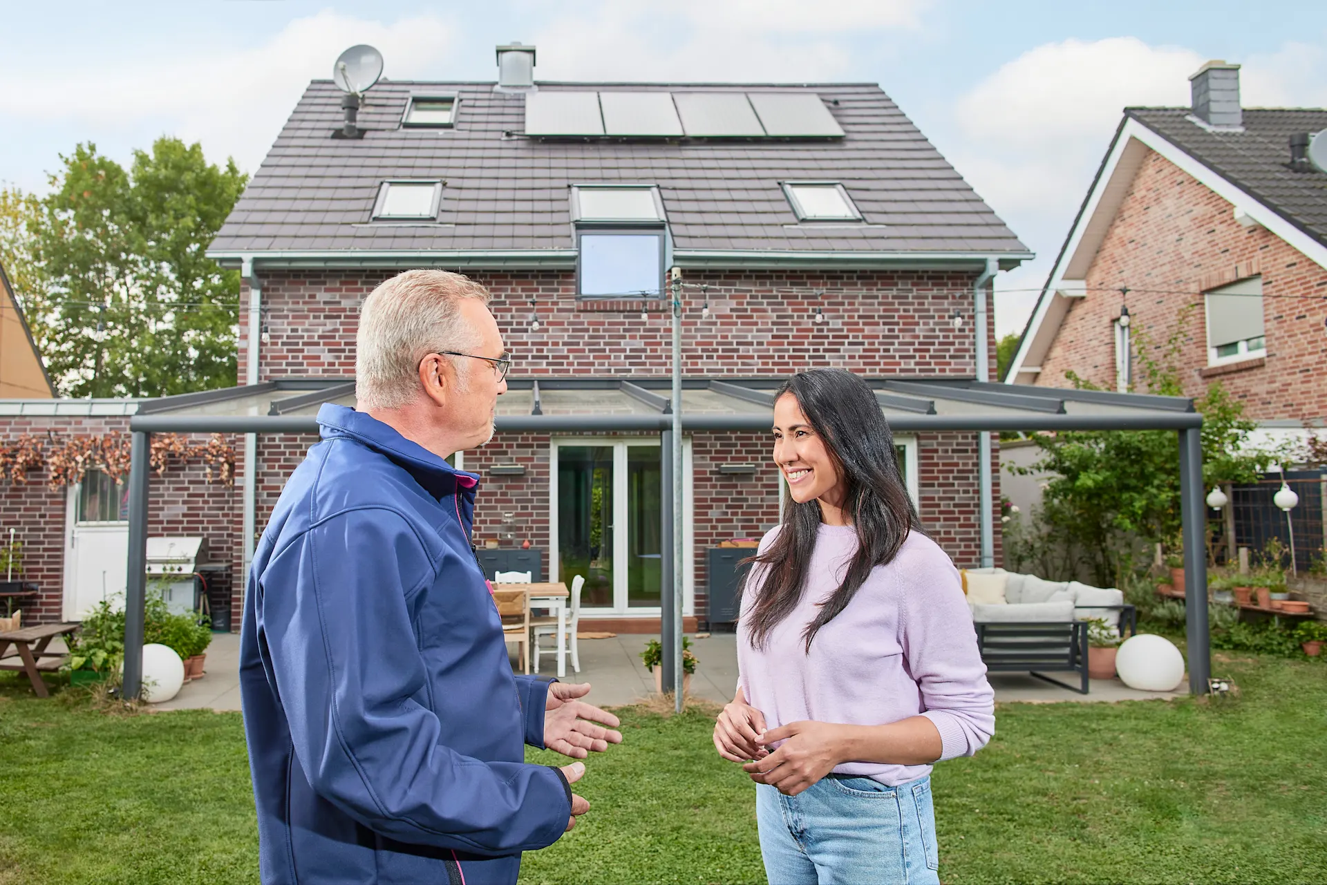 Ein NEW Mitarbeiter berät eine Kundin vor ihrem Einfamilienhaus bezüglich einer Photovoltaikanlage von der NEW Energie und grüner Energie.