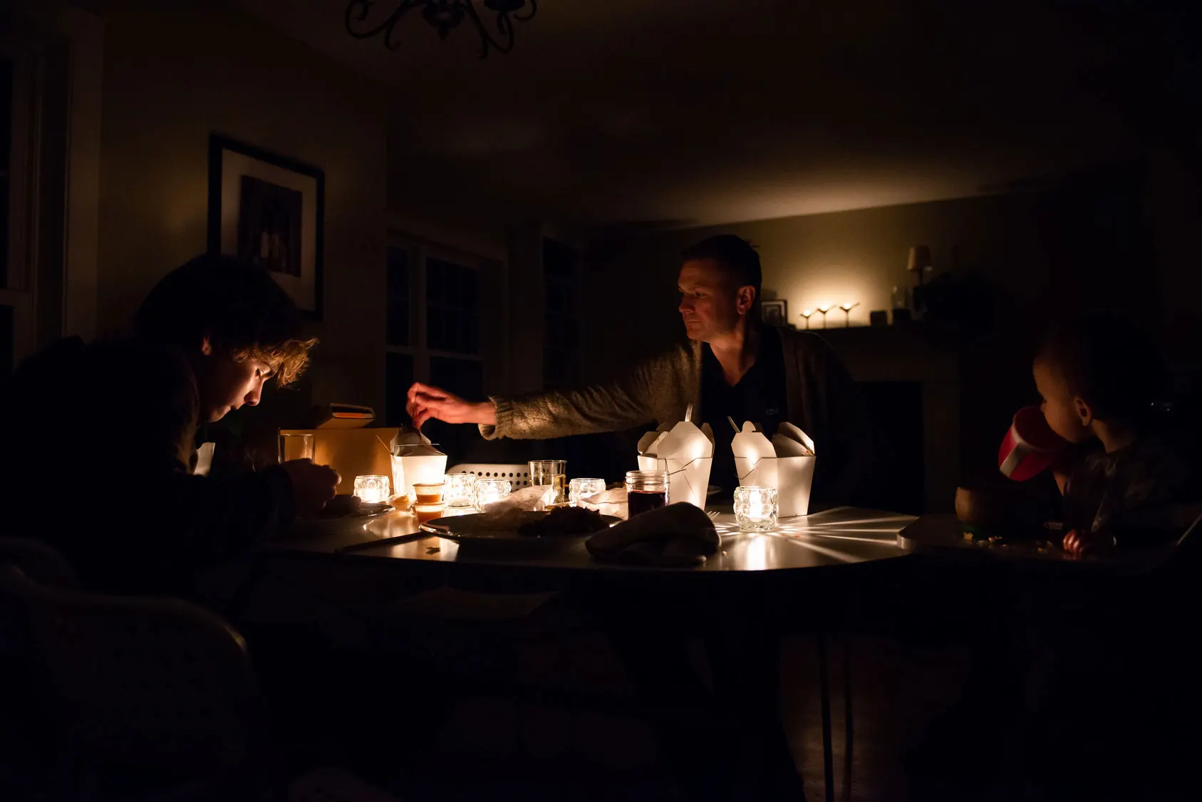 Länger anhaltender Stromausfall Familie sitzt nach einem Stromausfall im dunkeln mit Kerzen am Tisch.