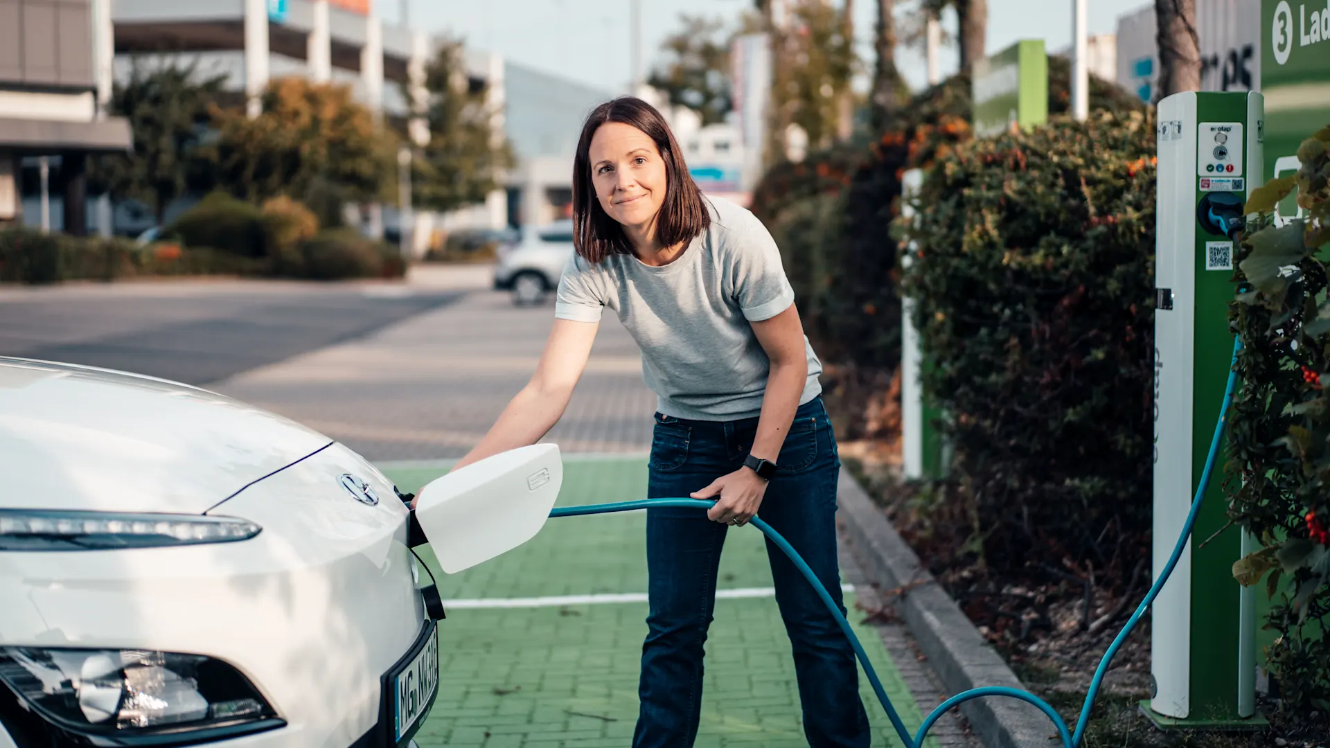 Laden des Elektroautos an öffentlicher Ladesäule Frau steht an einer Ladestelle zum Laden ihres E-Autos.