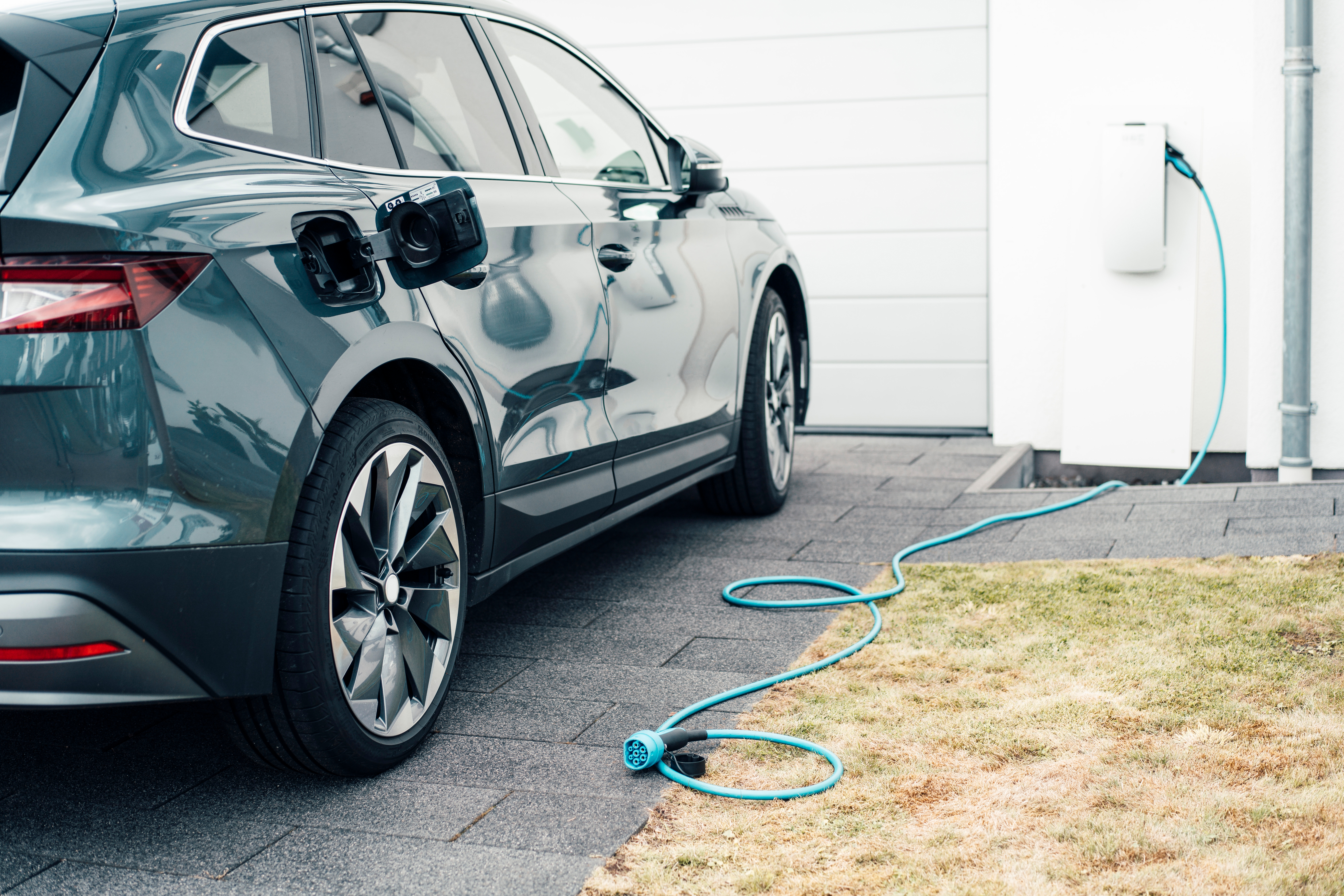 Ein Ladekabel hängt in einer Wallbox der NEW Energie. Ein E-Auto steht daneben.