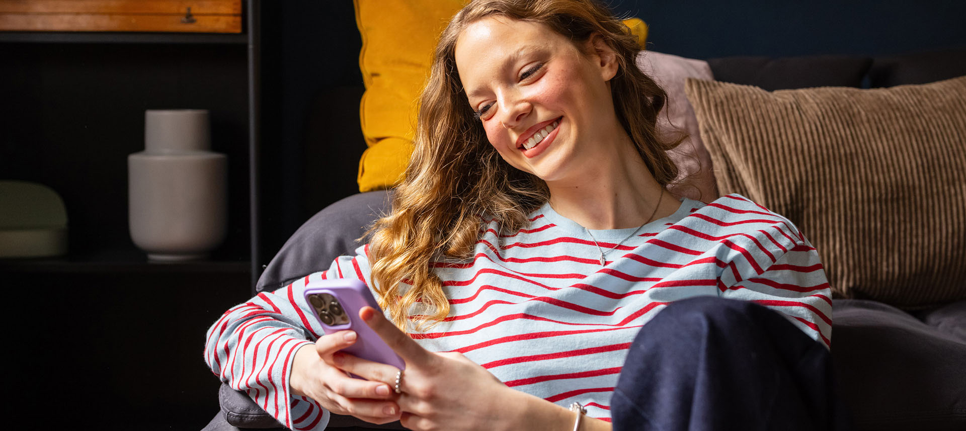 Eine Frau sitzt mit ihrem Smartphone auf dem Sofa und informiert sich über die günstigen Strom- und Gastarife bei der NEW Energie.