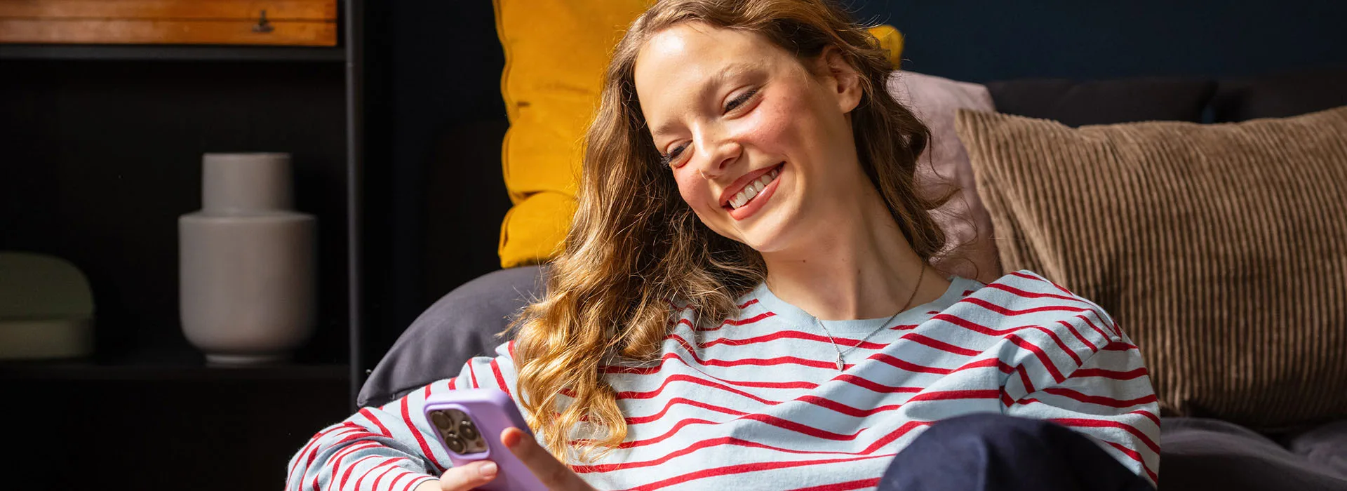 Strom und Gas von der NEW Energie Eine Frau sitzt mit ihrem Smartphone auf dem Sofa und informiert sich über die günstigen Strom- und Gastarife bei der NEW Energie.