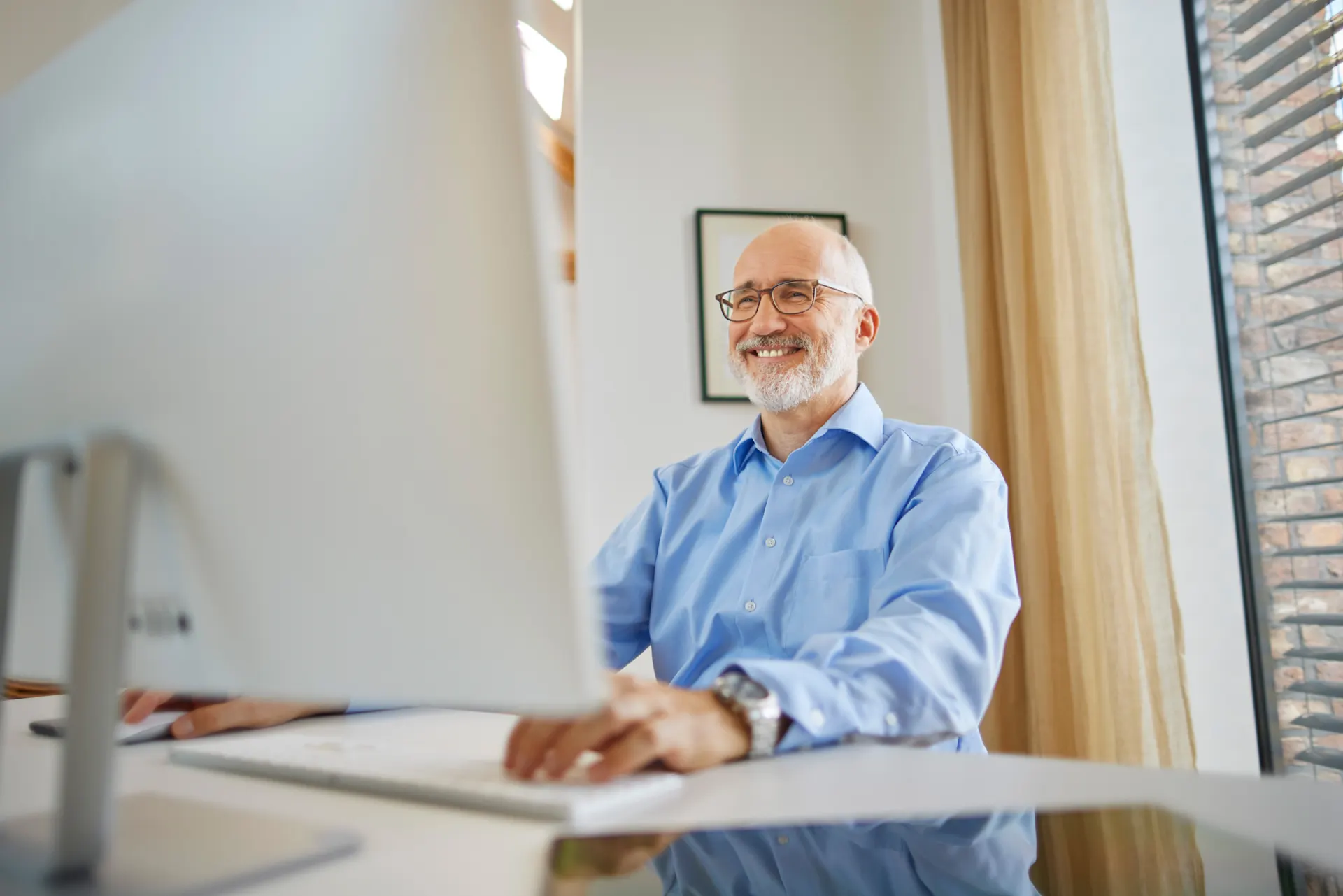 Ein Verwalter sitzt am Schreibtisch und erfreut sich an der Arbeit am Laptop.