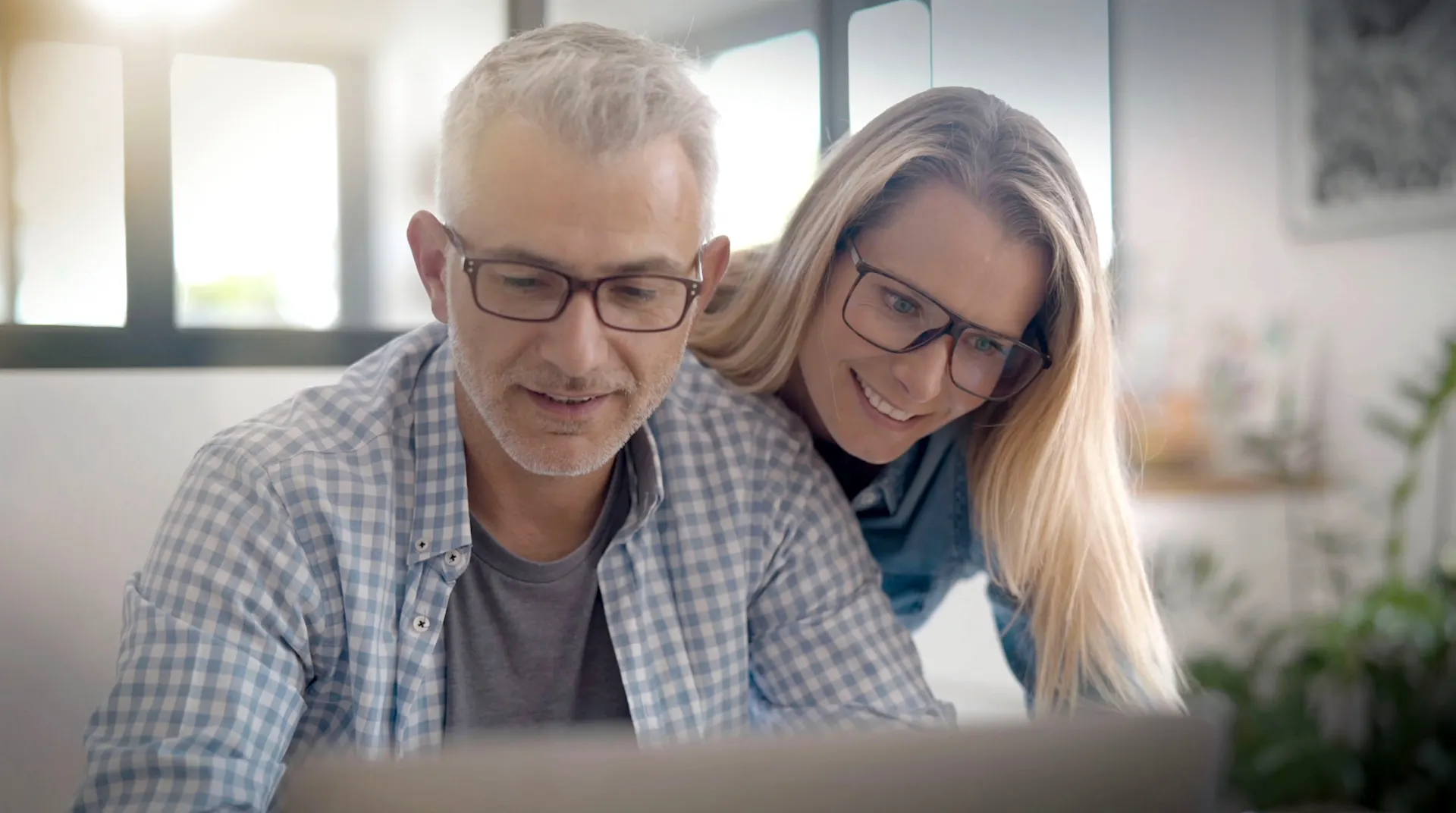 Eine Frau schaut ihrem Mann über die Schulter. Er arbeitet am Laptop und besucht die Seite von der NEW Energie.