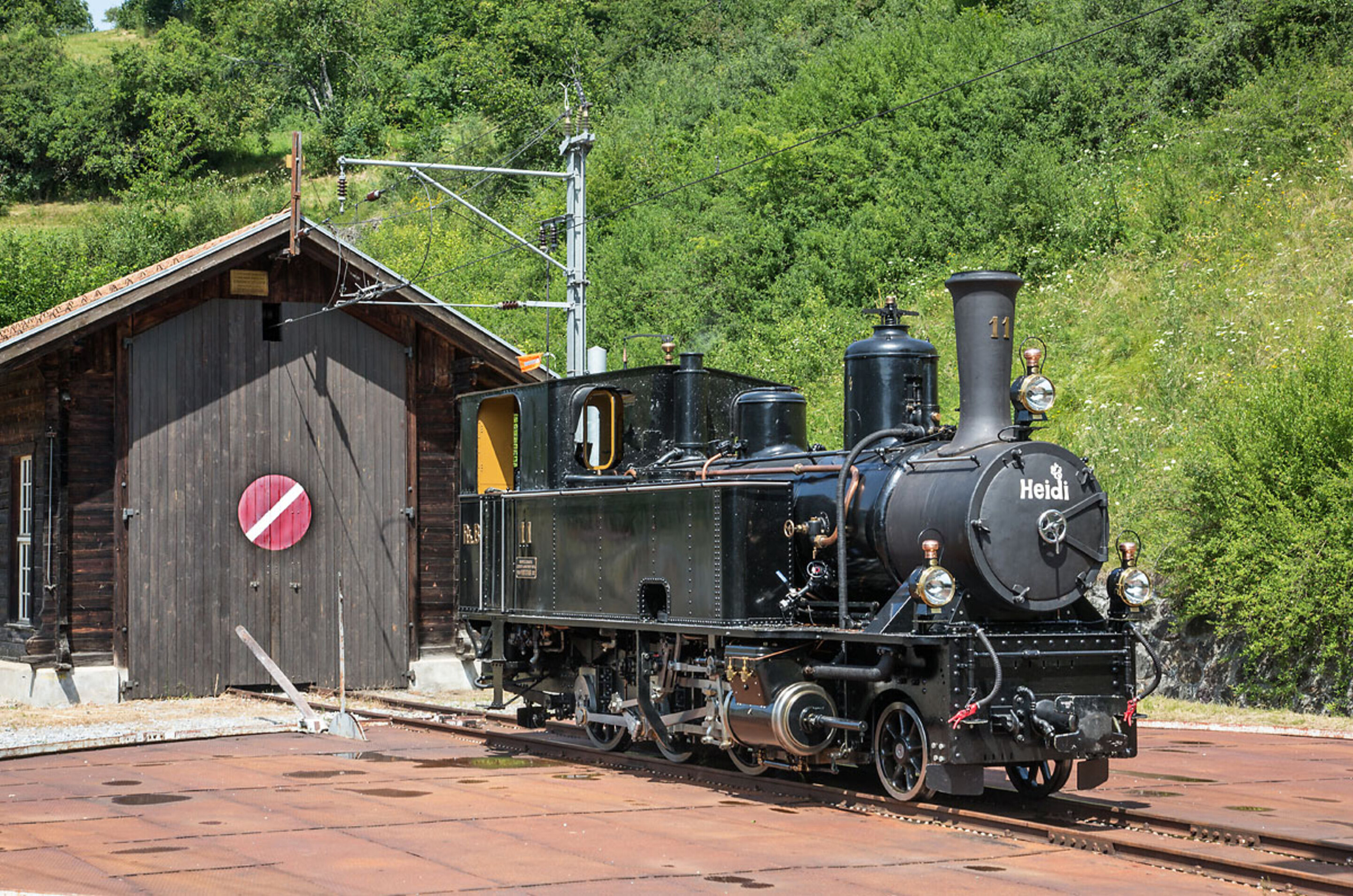 Die Dampflokomotive Heidi steht vor einem alten Bahnhof. 