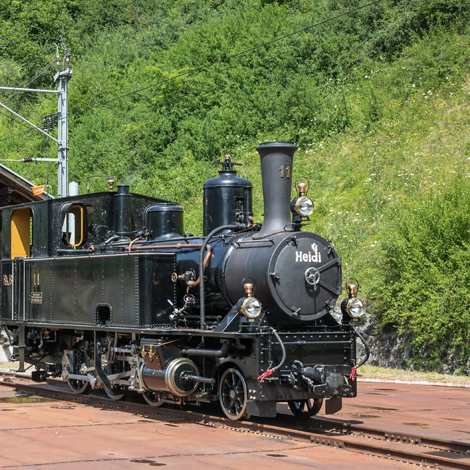 Die Dampflokomotive Heidi steht vor einem alten Bahnhof.