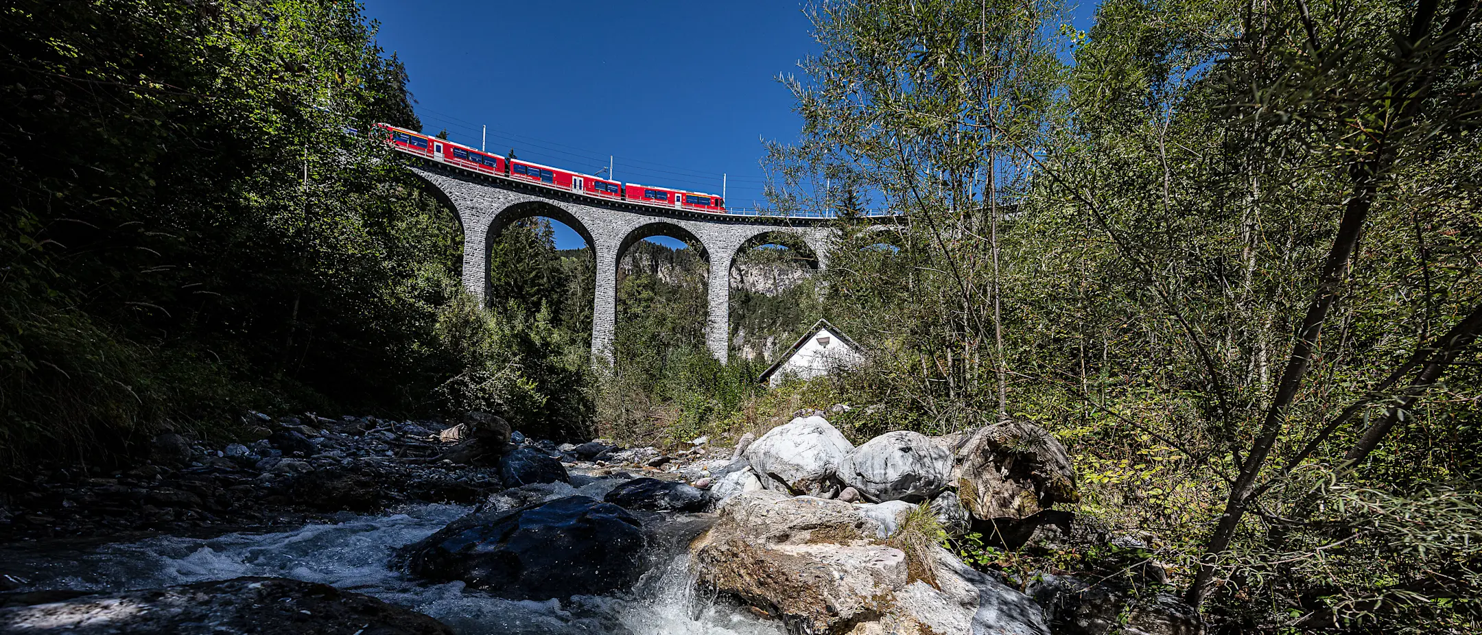 Allegra-Triebzug auf dem Schmittnertobelviadukt im Sommer mit Bach im Vordergrund.