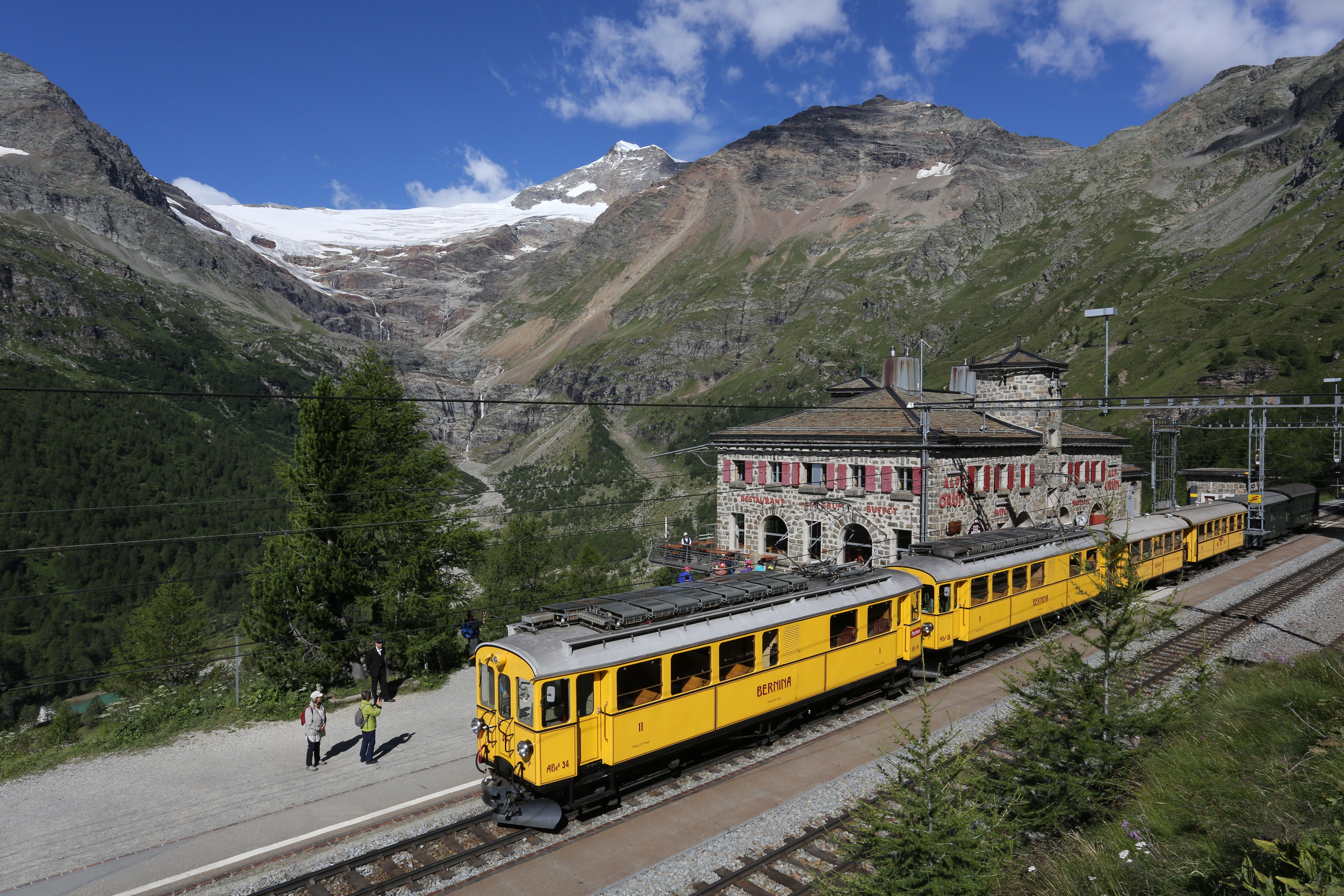 Historische Bernina Triebwagen stehen am Bahnhof Alp Grüm. Im Hintergrund ist der Gletscher zu sehen. 