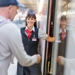 Eine Zugbegleiterin zeigt einem Fahrgast den Weg in den Zug
