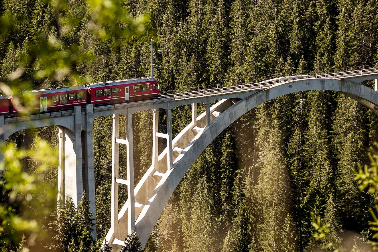 Un treno regionale rosso della Ferrovia retica attraversa l’imponente viadotto di Langwies nel cuore delle Alpi.