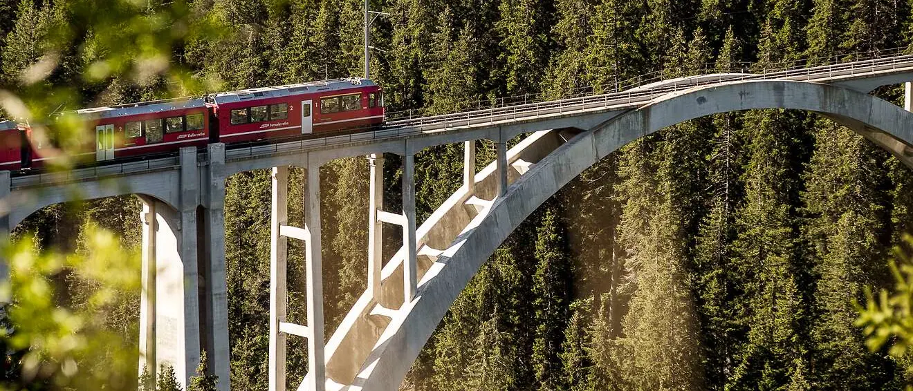 Ein roter Regionalzug der Rhätischen Bahn überquert den imposanten Langwieserviadukt, inmitten der Alpen.