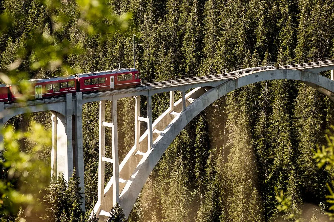 Ein roter Regionalzug der Rhätischen Bahn überquert den imposanten Langwieserviadukt, inmitten der Alpen.