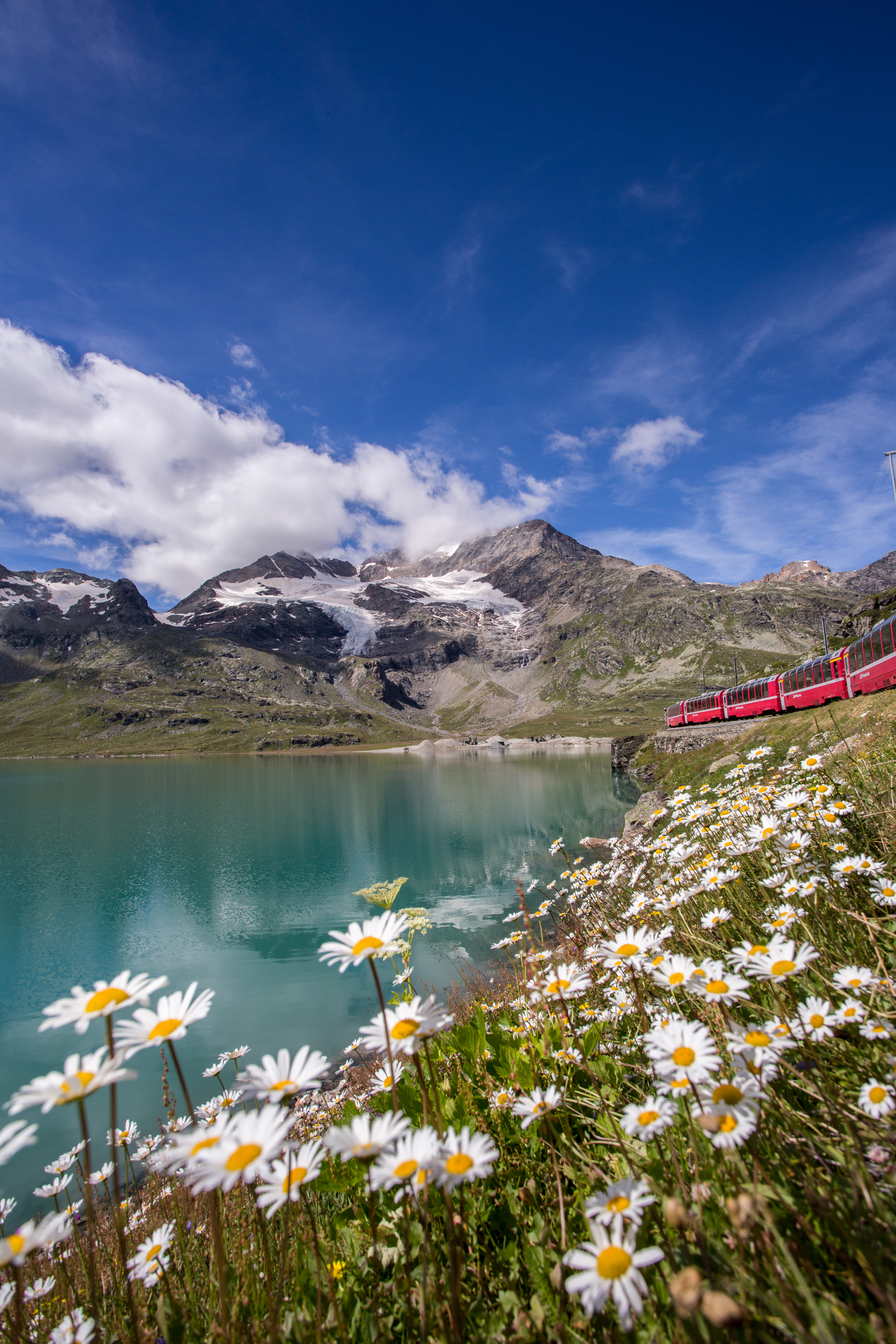 The Bernina Express travels along the turquoise Lago Bianco, with glaciers and mountains in the background.