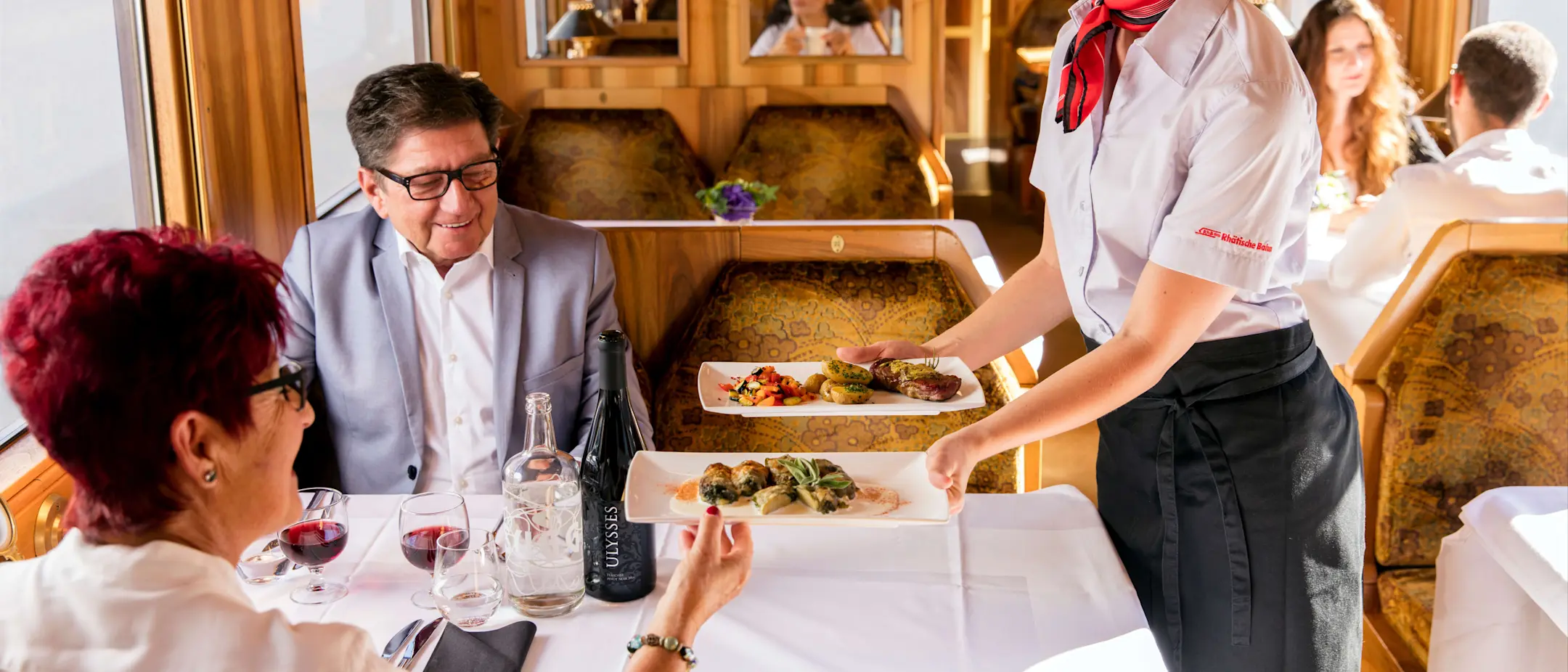 Servicemitarbeiterin der Rhätischen Bahn schenkt Wein bei einer festlichen Fahrt in einem nostalgischen Speisewagen ein.