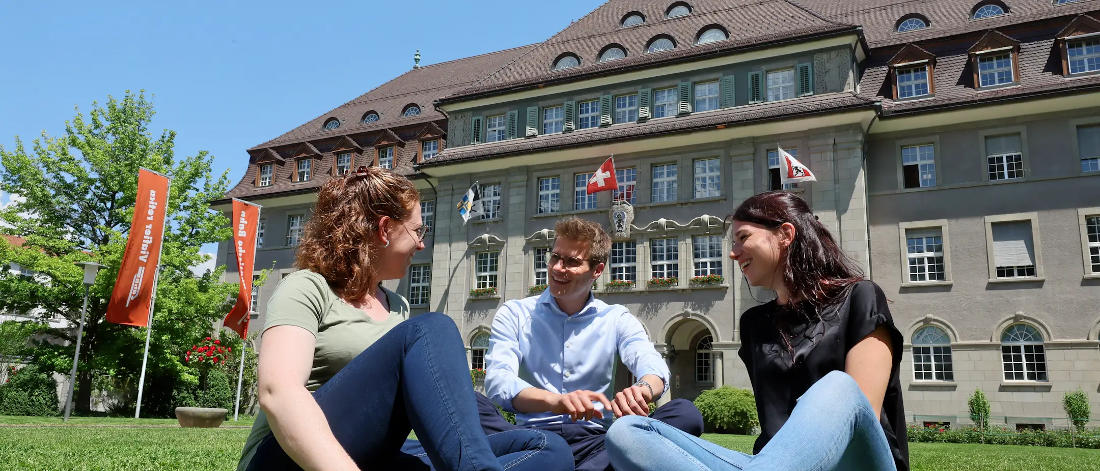 Drei Mitarbeitende der RhB sitzen im Sommer auf der Wiese vor der RhB-Zentrale