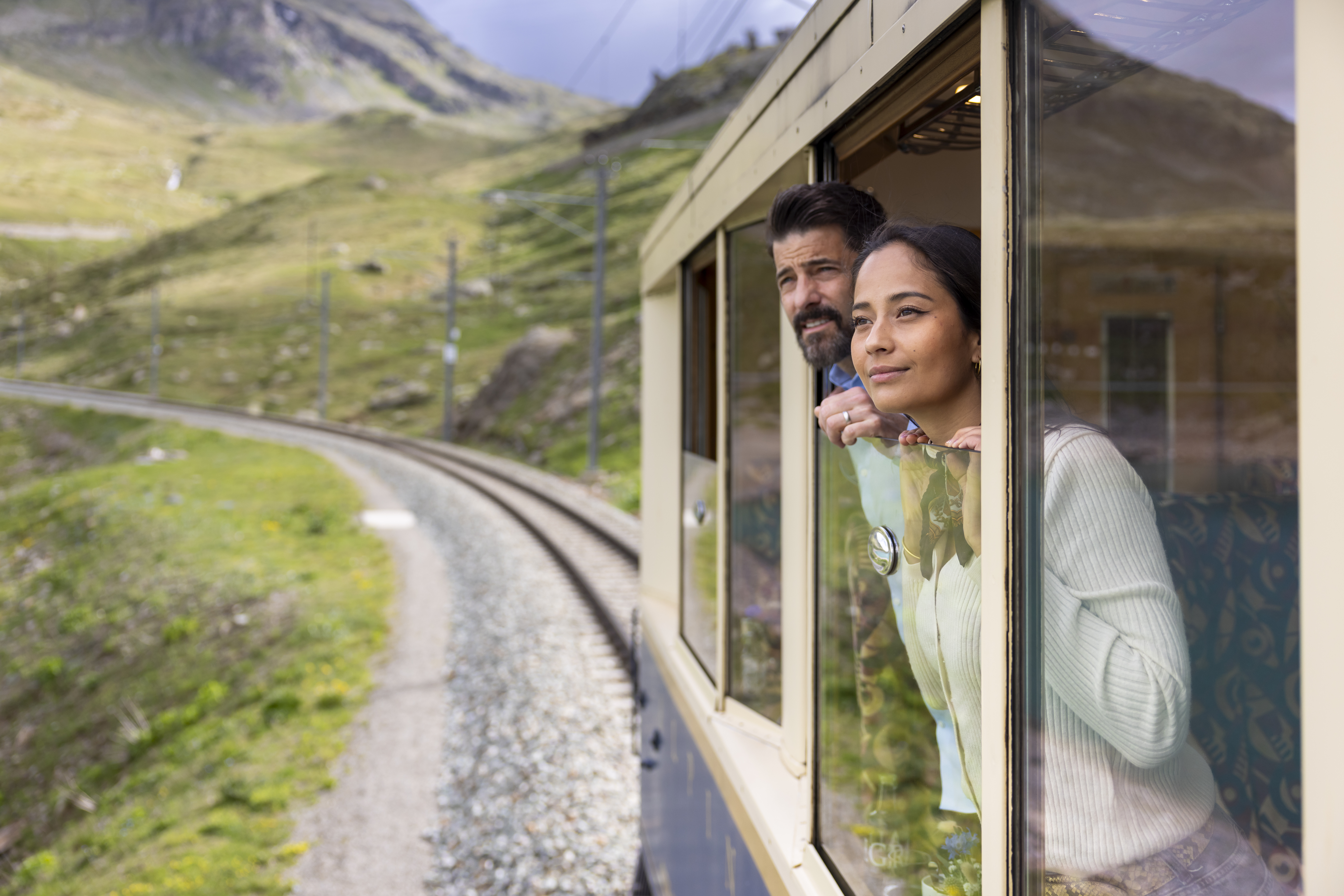 Zwei Personen schauen aus dem nostalgischen Wagen in die Bündner Landschaft. 