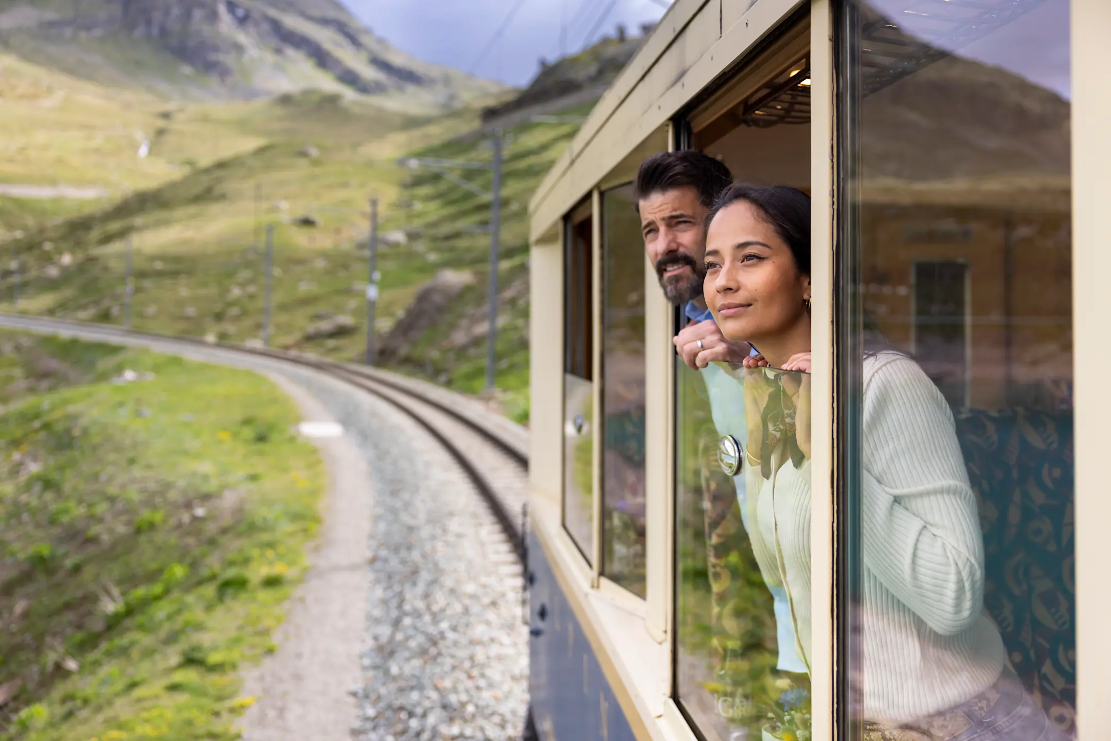 Zwei Personen schauen aus dem nostalgischen Wagen in die Bündner Landschaft.
