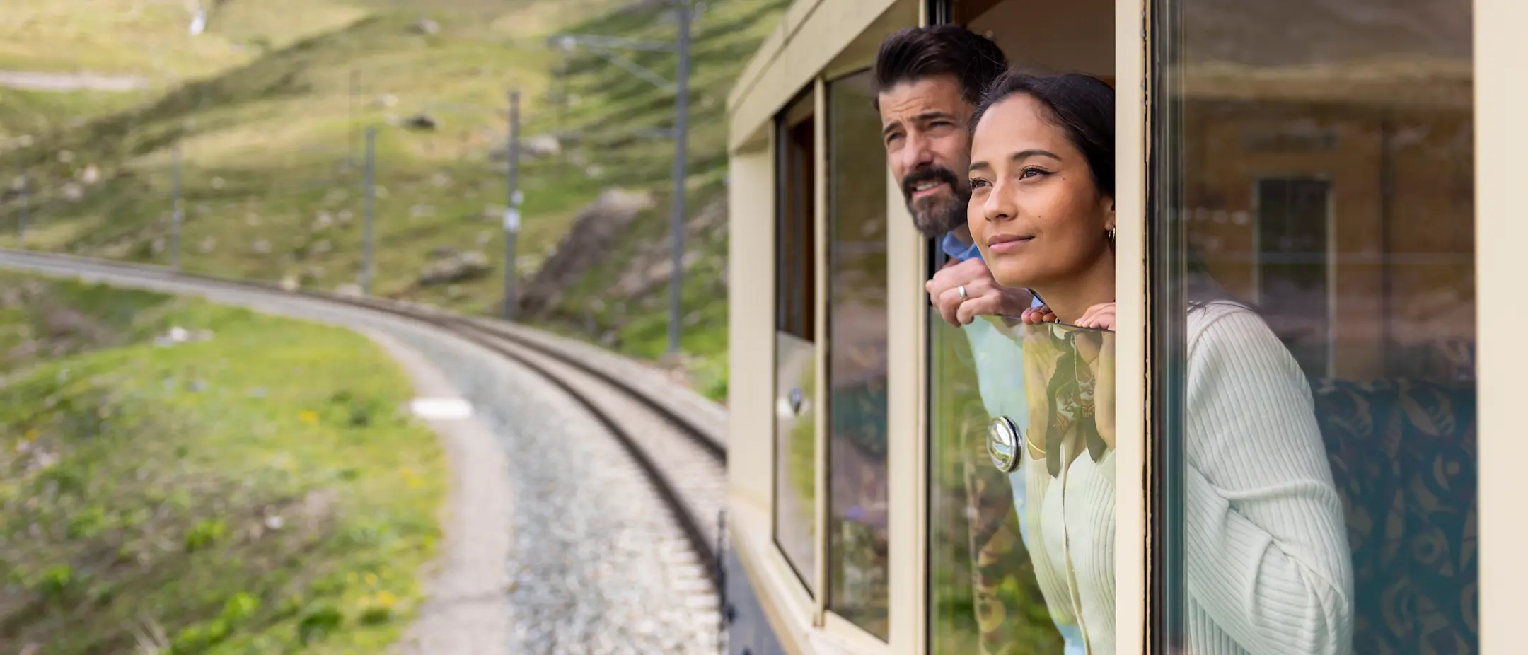 Zwei Personen schauen aus dem nostalgischen Wagen in die Bündner Landschaft.